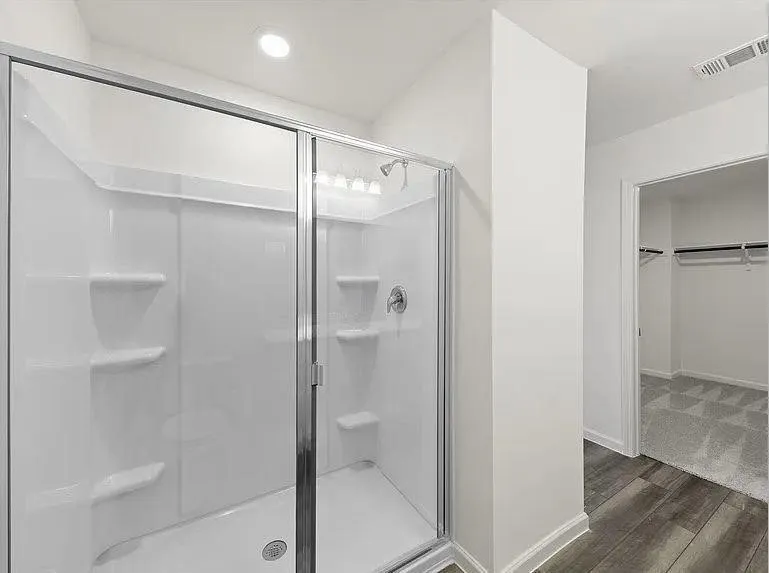 Walk-in shower with clear glass enclosure and integrated shelving, featuring a chrome shower head and fixtures
