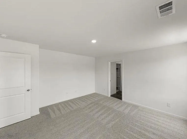 Spacious room featuring light gray patterned carpeting, recessed lighting, white walls, and a white interior door with panel detailing