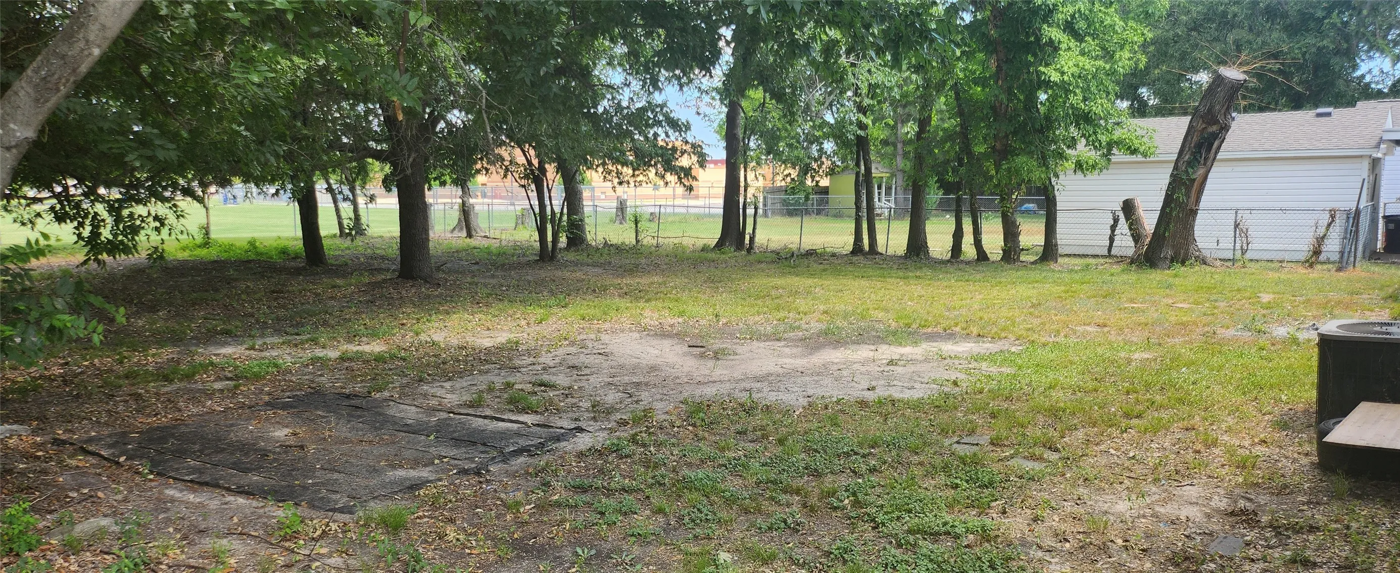 Expansive backyard featuring mature trees, a chain-link fence, and a concrete pad