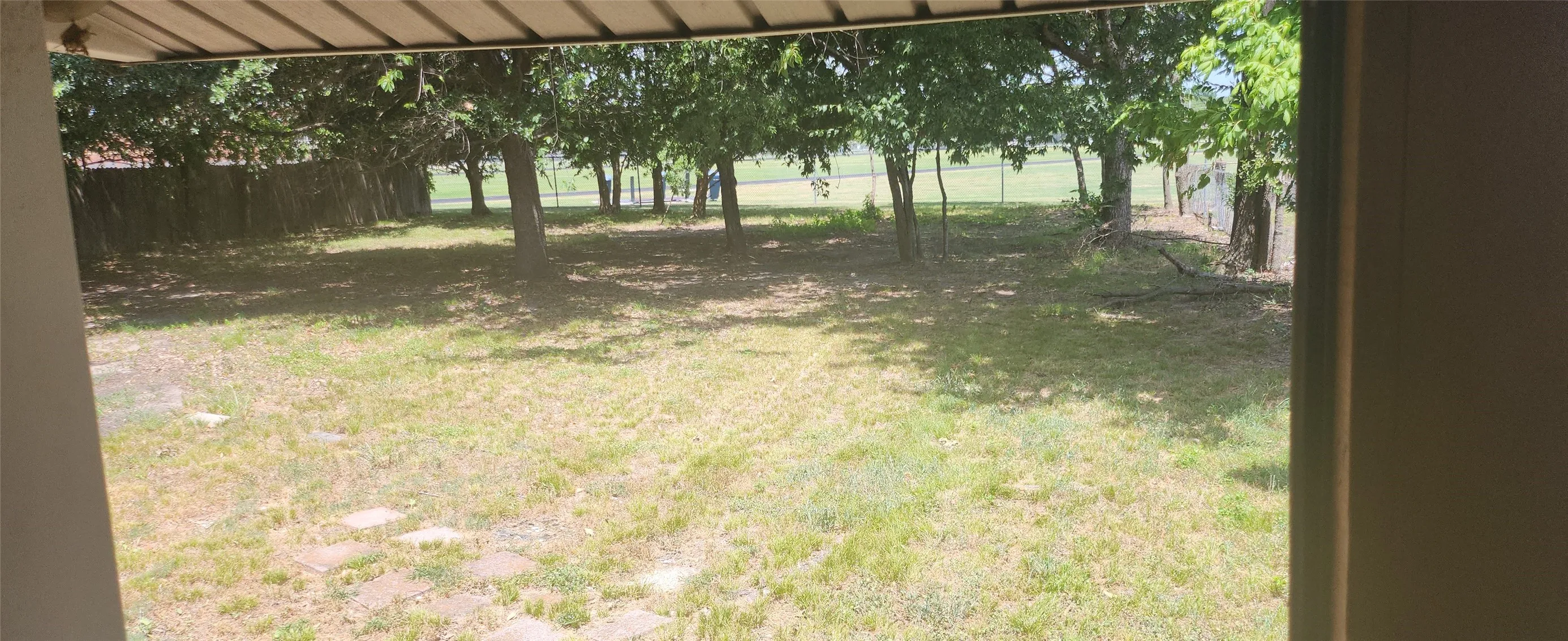Expansive grassy area featuring mature trees and a chain-link fence