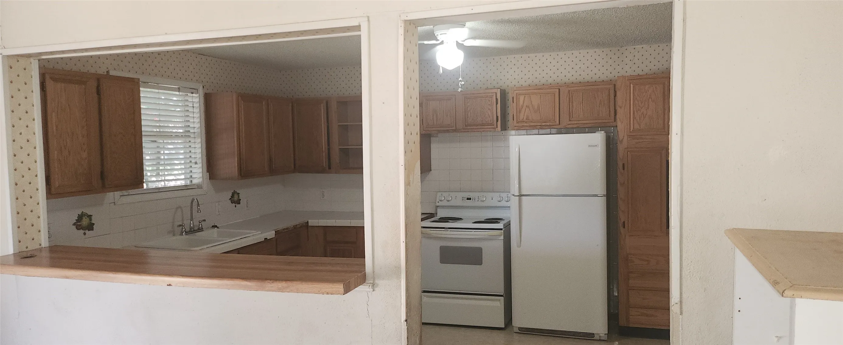 Kitchen with wood-finish cabinetry, white appliances, and a pass-through window with a wood-finish bar top