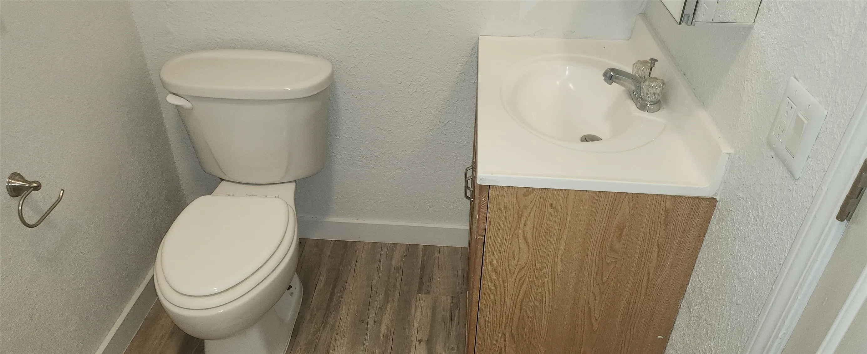 Bathroom featuring a white toilet, wood-finish vanity with an integrated sink, and wood-finish flooring