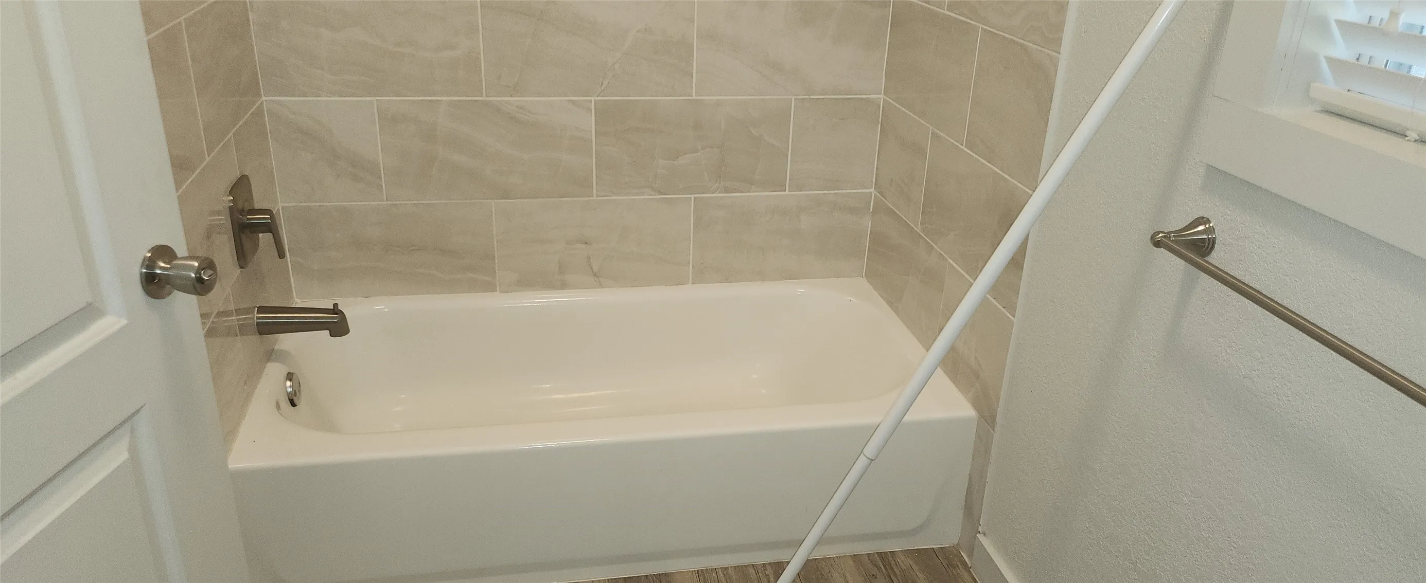 Bathtub with surrounding tile enclosure, brushed nickel faucet, and wood-finish flooring
