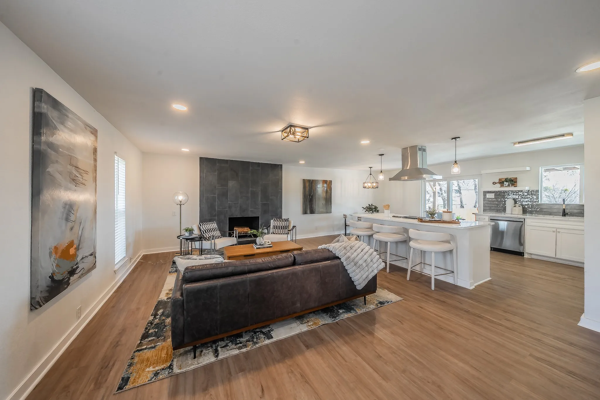 Open-concept living space featuring wood-finish flooring, a stone-clad fireplace, recessed lighting, and a kitchen island with pendant lighting