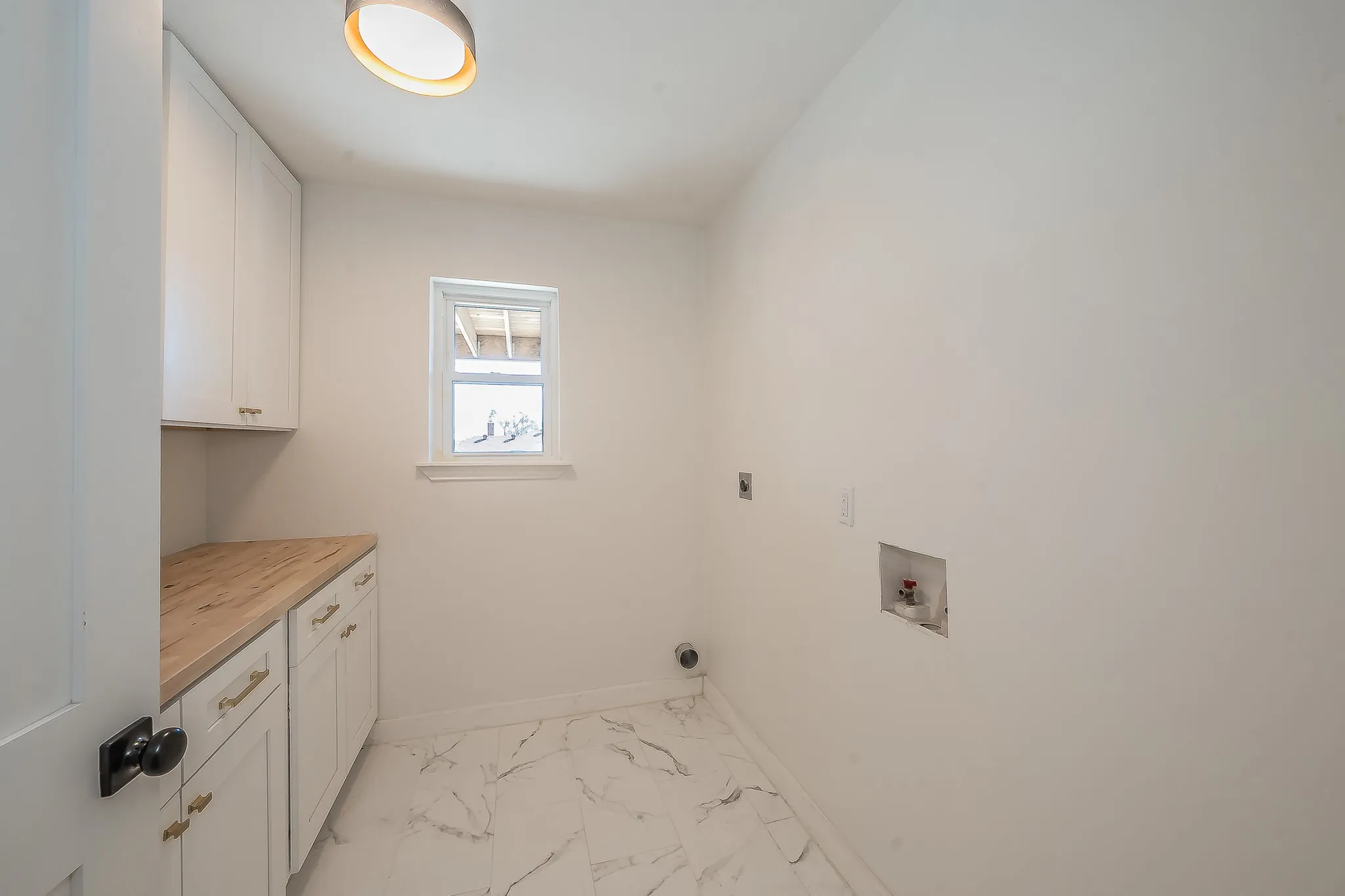 Utility space featuring white cabinetry with gold-tone hardware, wood-finish countertops, and marble-look floor tiling