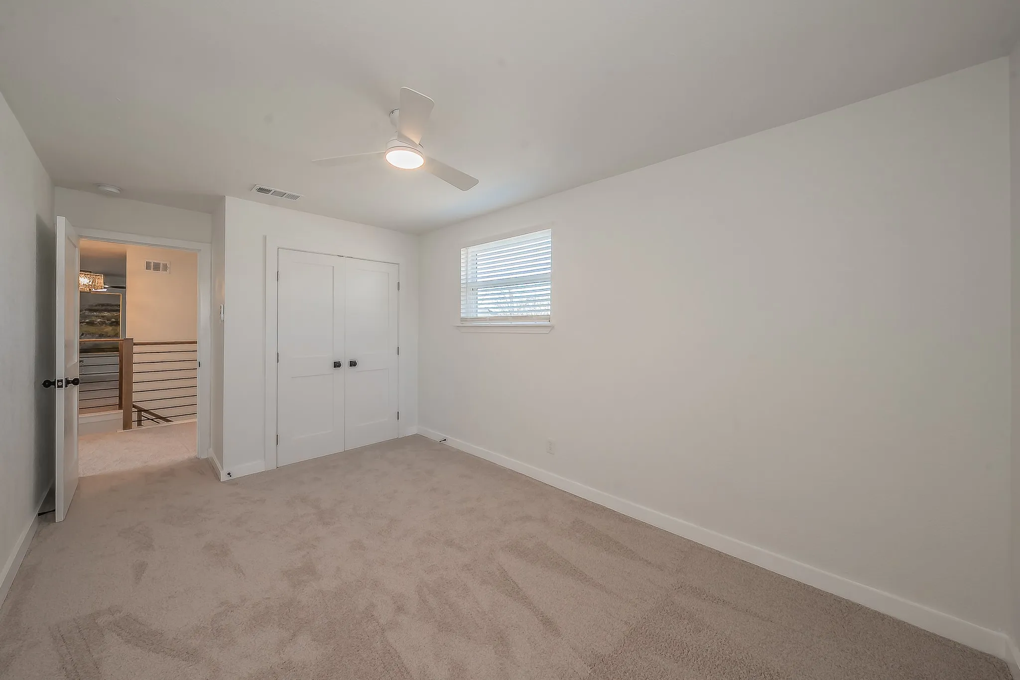 Neutral-toned carpeted room featuring a ceiling fan with integrated lighting, a window with horizontal blinds, and a double-door closet with black hardware