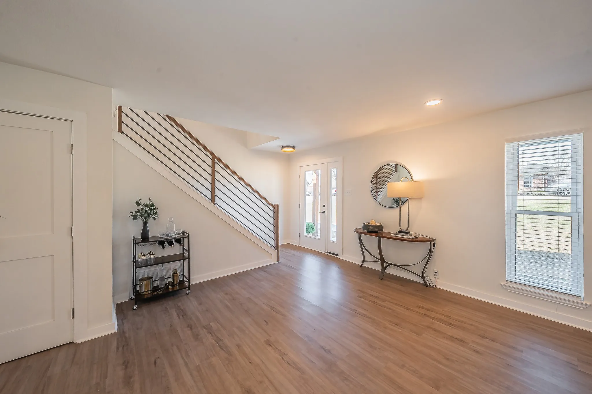 Spacious entry area featuring wood-finish flooring, a contemporary staircase with horizontal metal balusters, recessed lighting, and a white paneled door