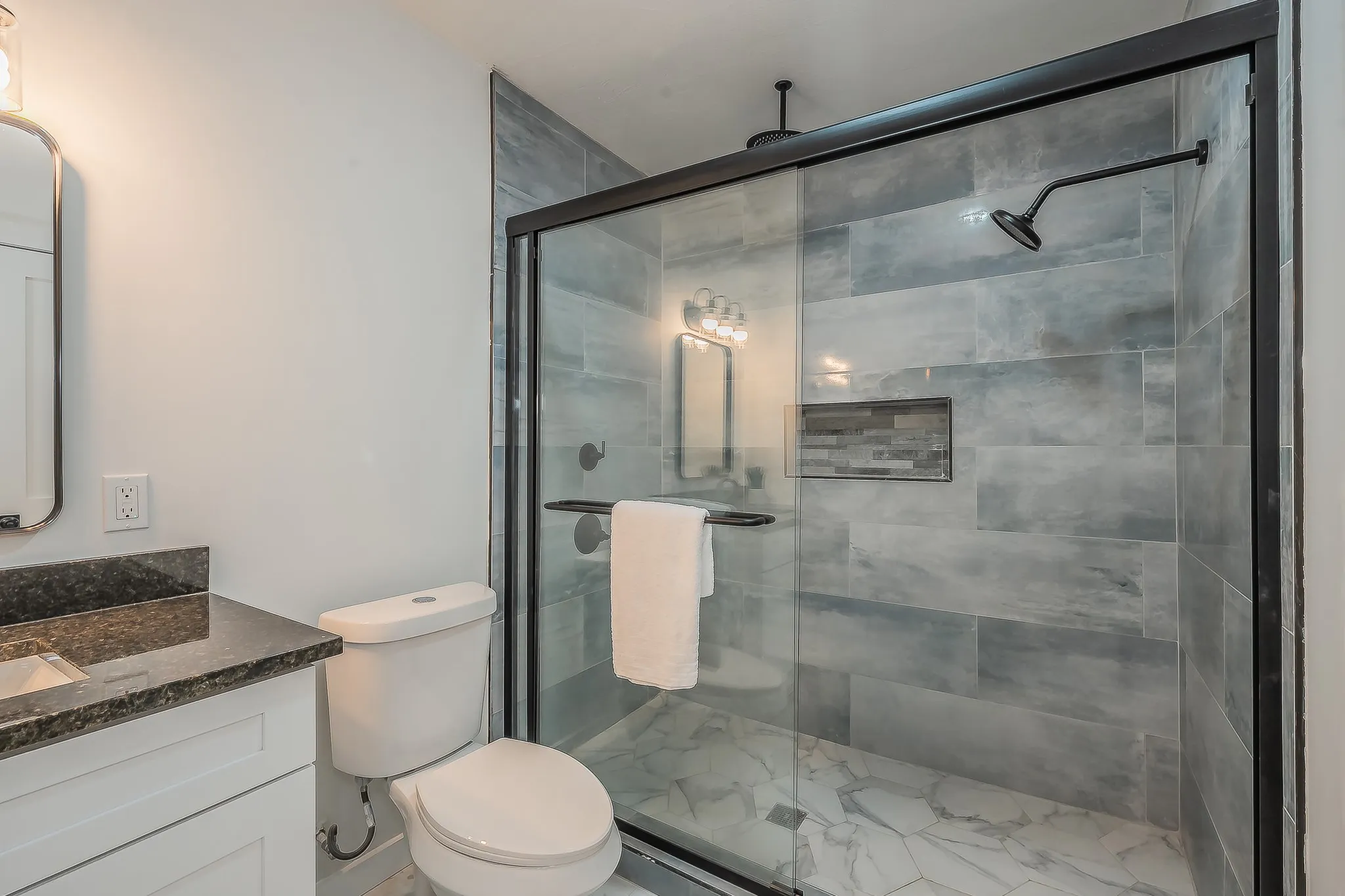 Walk-in shower featuring a matte black framed glass enclosure, a matte black shower head, and gray tile walls