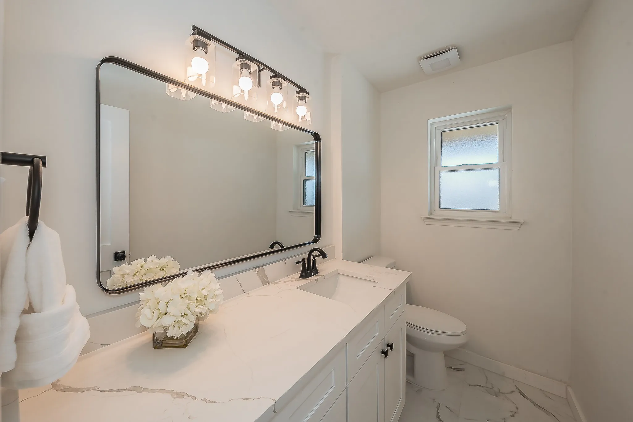 Contemporary bathroom featuring a spacious vanity with white cabinetry, a light-toned countertop with veining, and a rectangular undermount sink