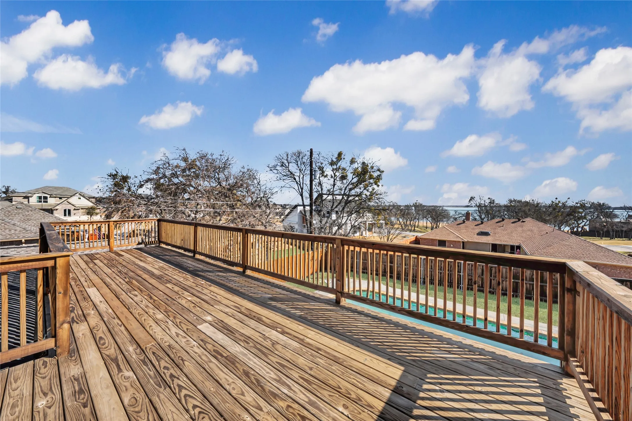 Expansive wood deck with natural wood railing overlooking a residential area and distant body of water