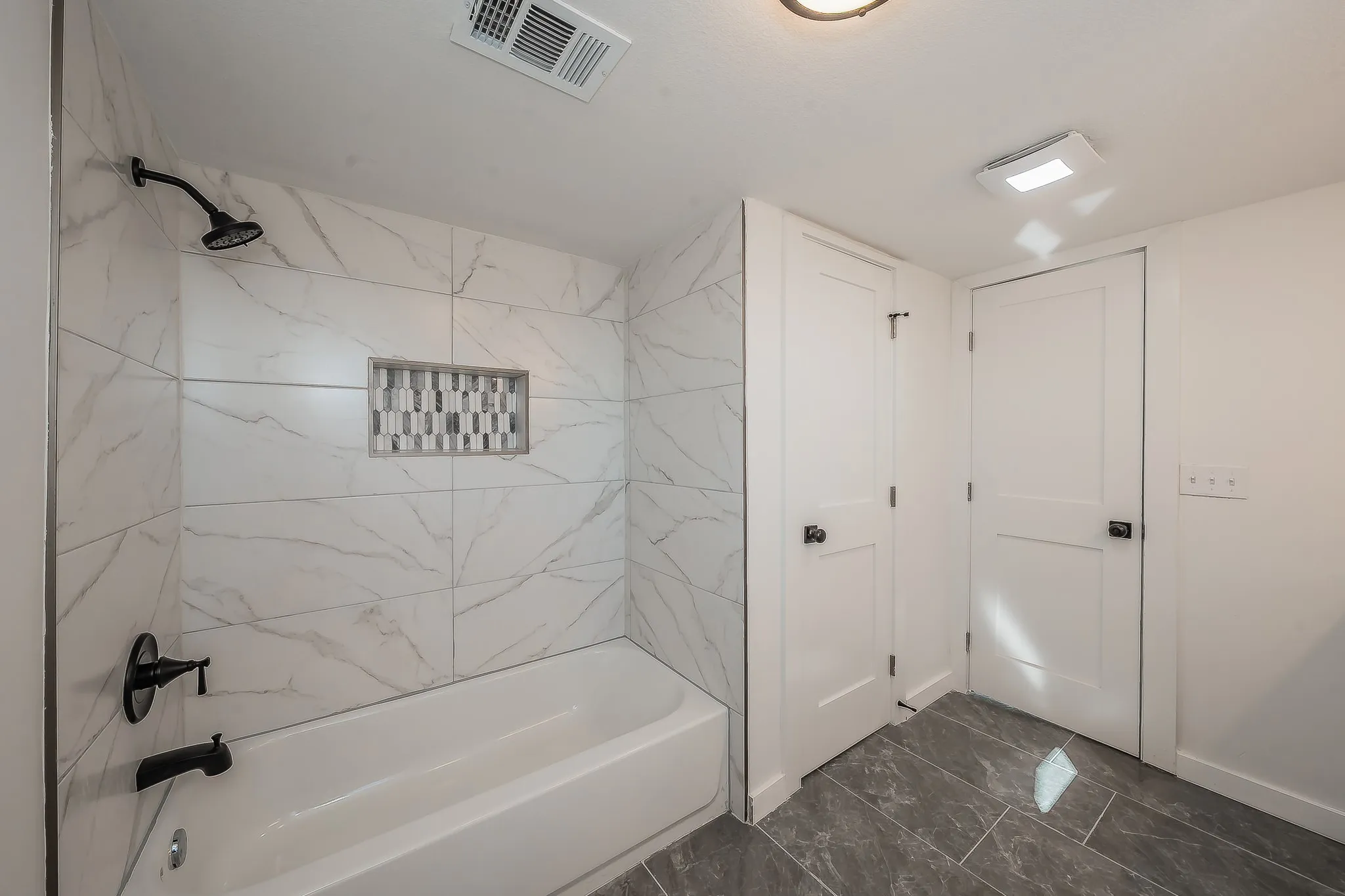Bathroom featuring a tiled tub-shower combination with matte black fixtures and a mosaic-tiled shower niche