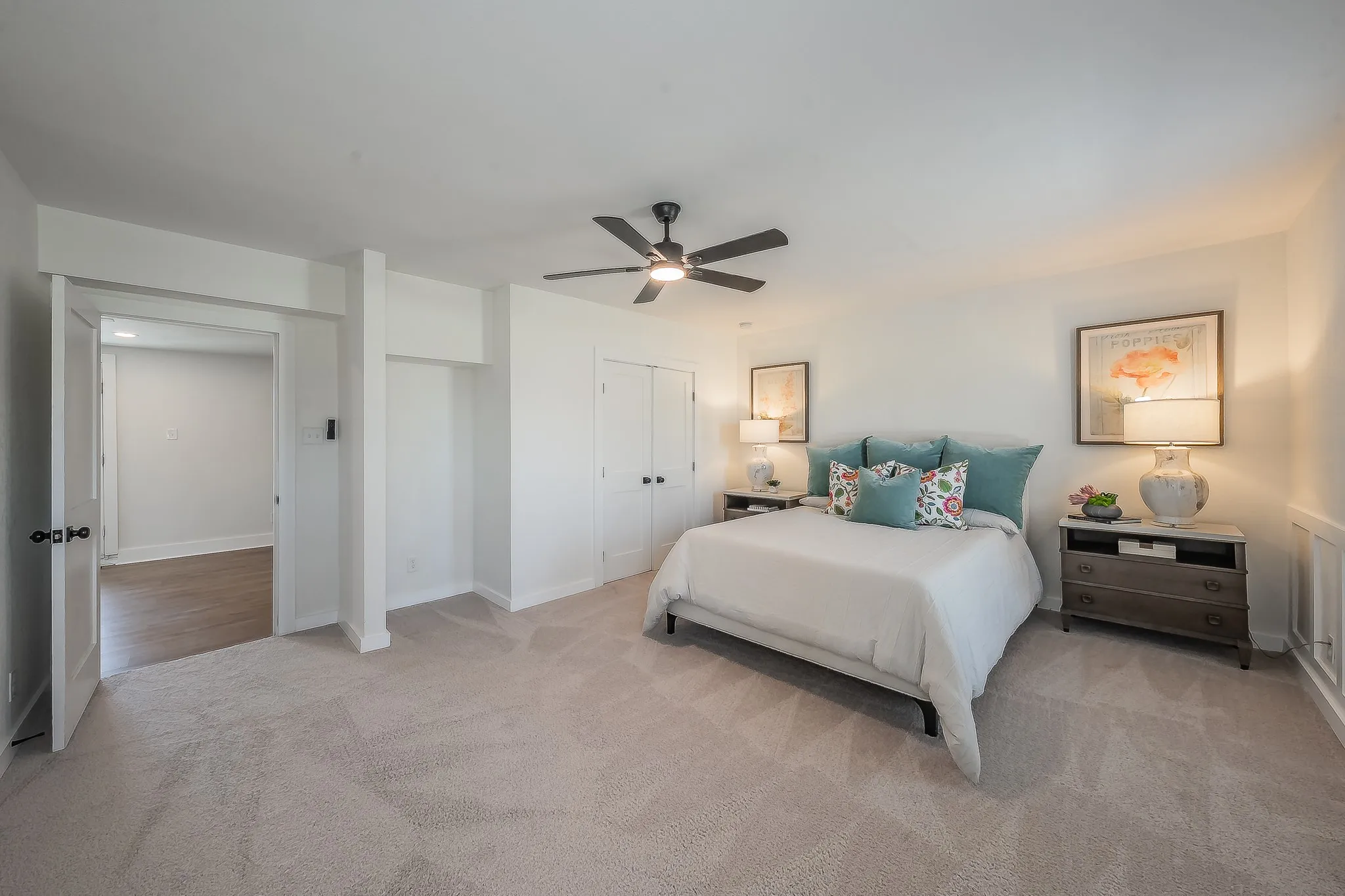 Spacious room featuring neutral carpeting, white walls, a ceiling fan, and double bi-fold doors