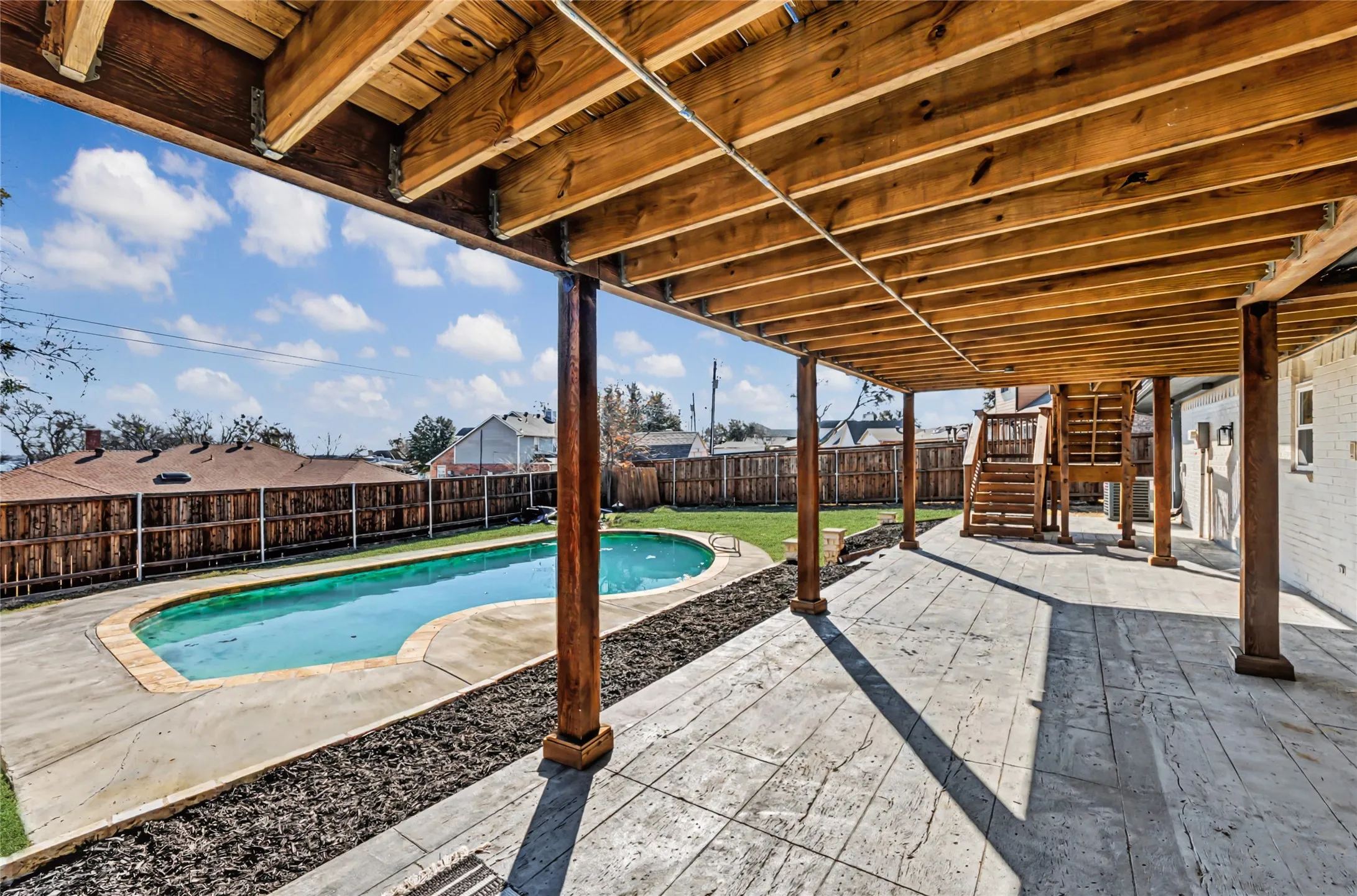 Expansive backyard featuring a kidney-shaped swimming pool, stamped concrete patio, wood privacy fencing, and a multi-level wood deck structure