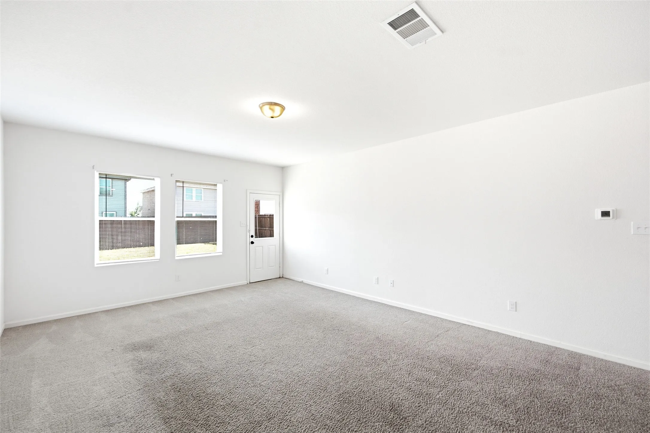 Neutral wall paint, light-toned carpeting, dual windows, and a rear door with a frosted insert