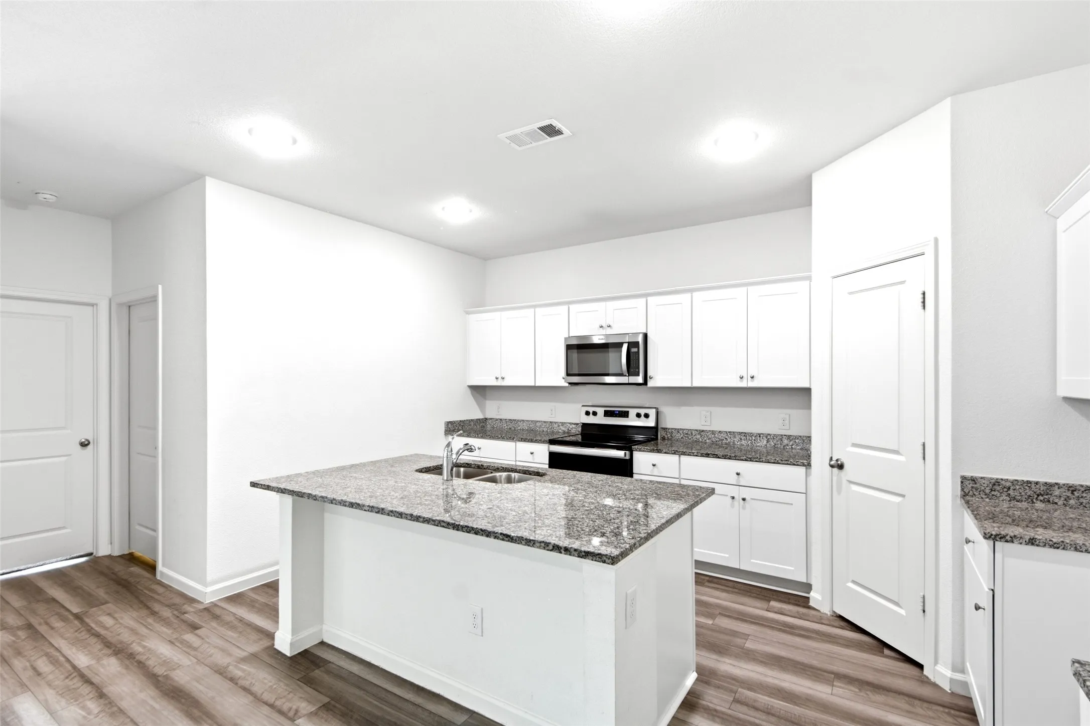 Kitchen featuring white cabinetry, stainless steel appliances, speckled stone countertops, and a central island with an integrated sink