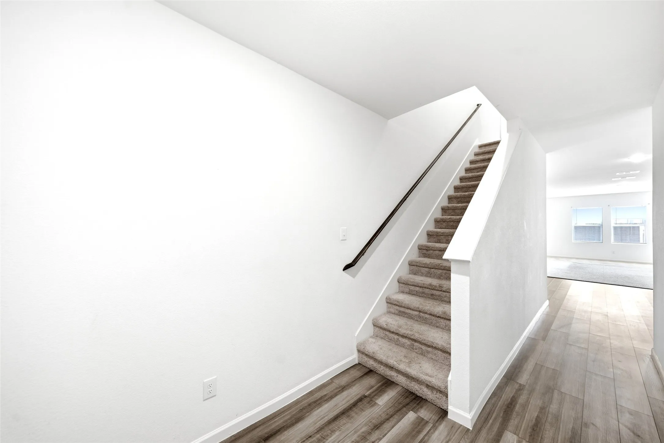 Staircase with carpeted treads, wood-finish flooring, and a black handrail