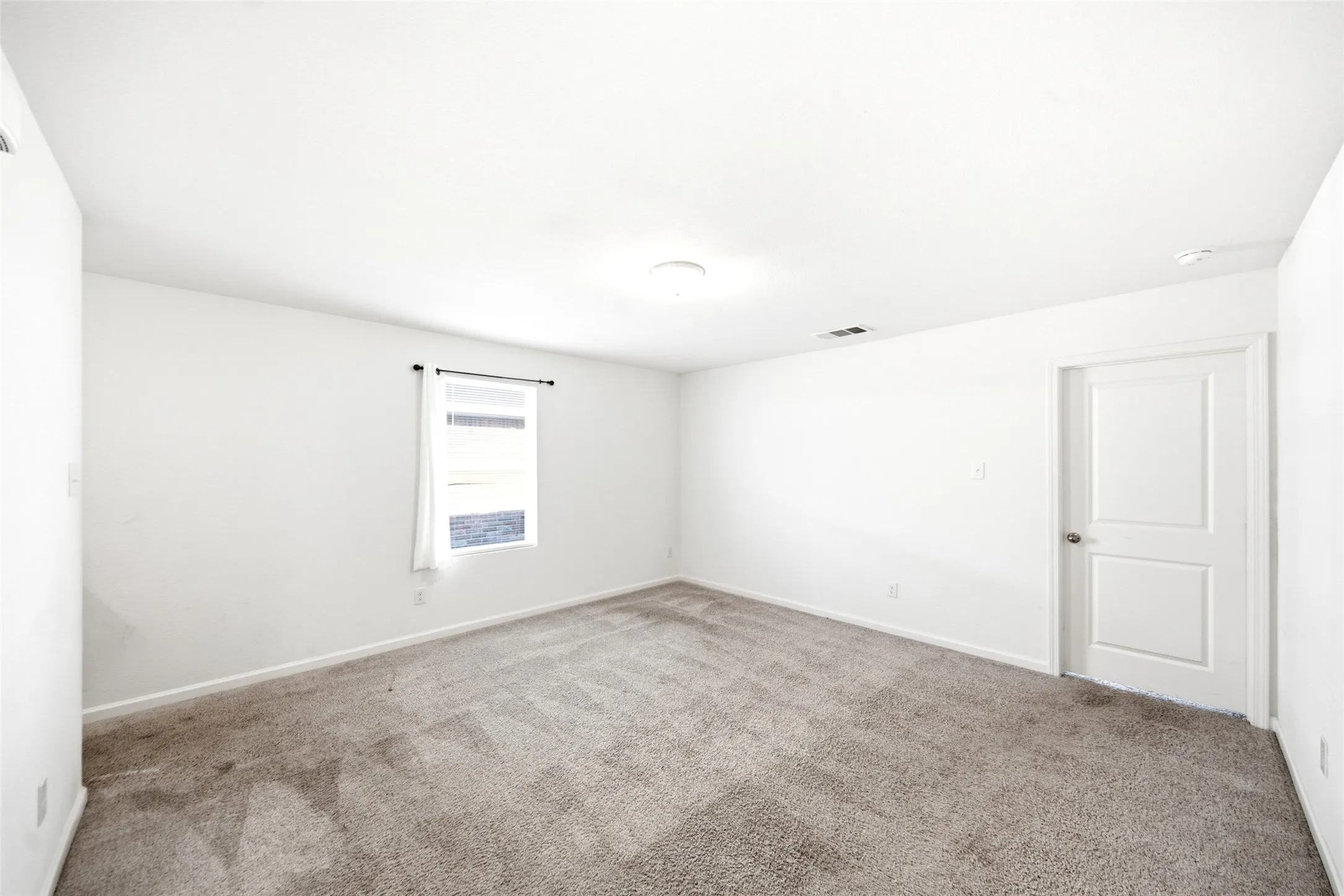 Neutral-toned carpeting, white painted walls, and a single window with a dark curtain rod