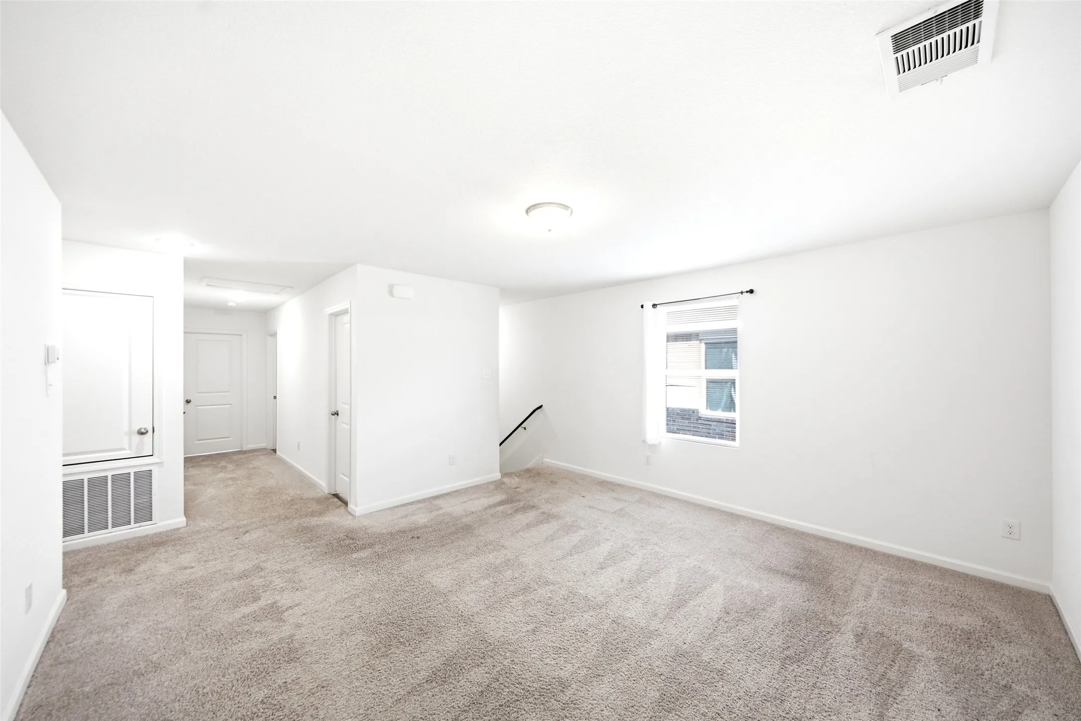 Neutral tone wall paint, neutral tone carpeting, ceiling-mounted light fixture, window with curtains, and interior doors