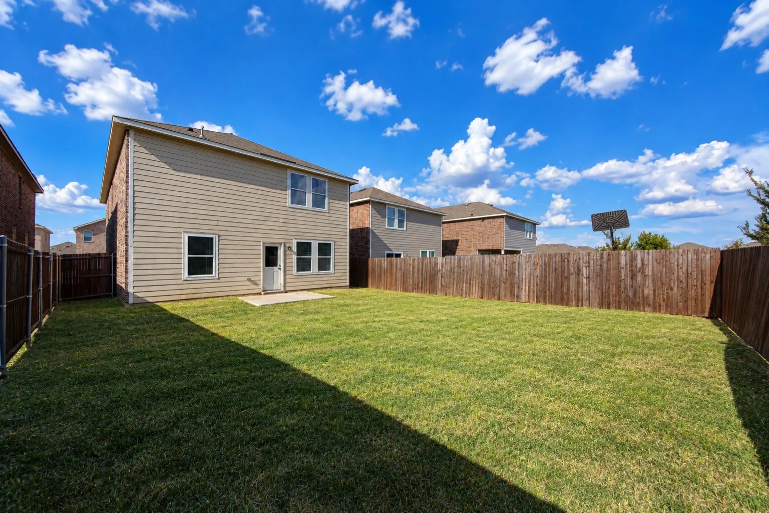 Expansive backyard featuring a manicured lawn, full wood fencing, and a concrete patio
