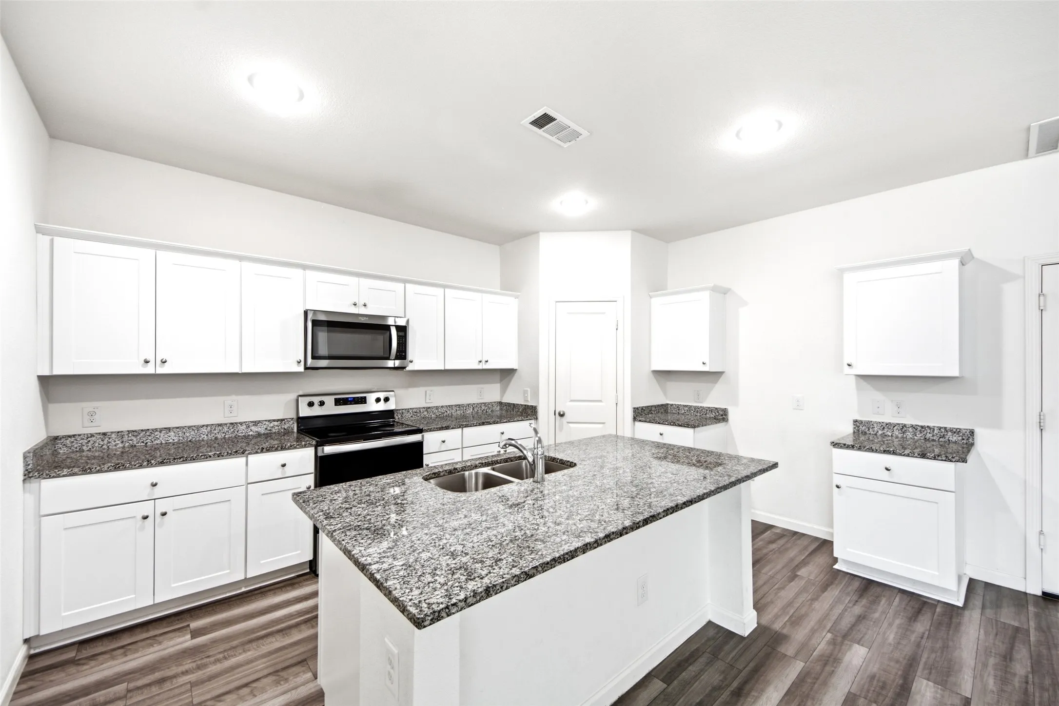 Kitchen with white cabinetry, granite countertops, stainless steel appliances, and wood-finish flooring