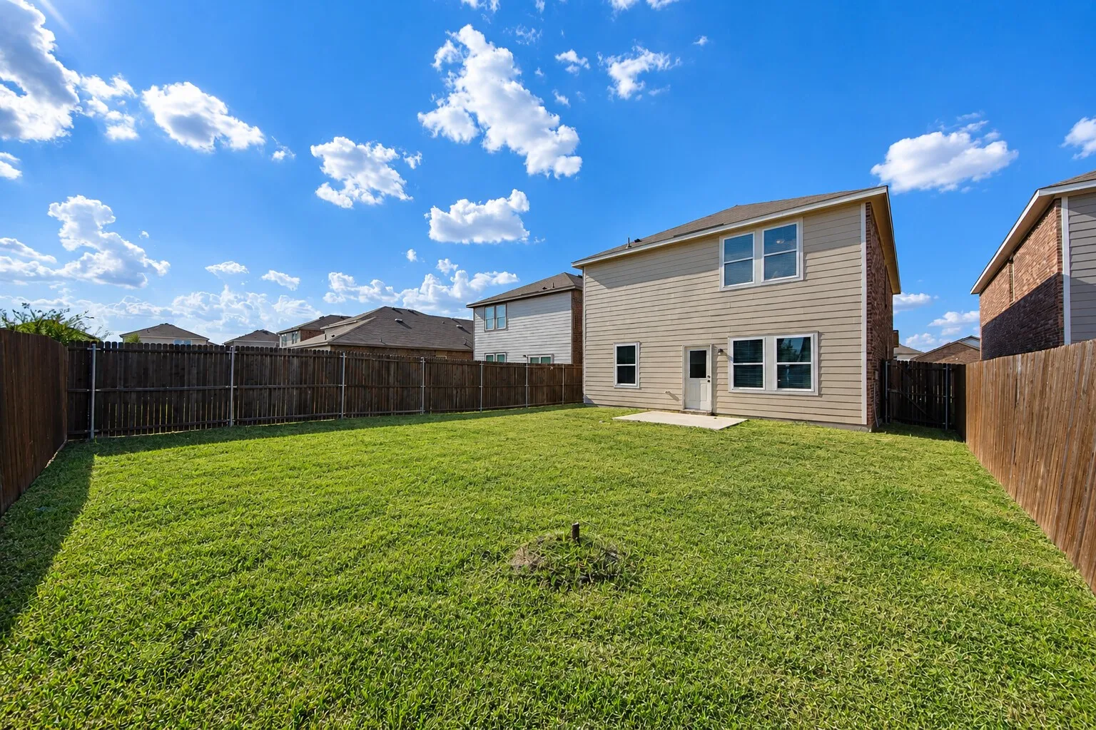 Expansive backyard with a manicured lawn, full wood privacy fencing, and a concrete patio