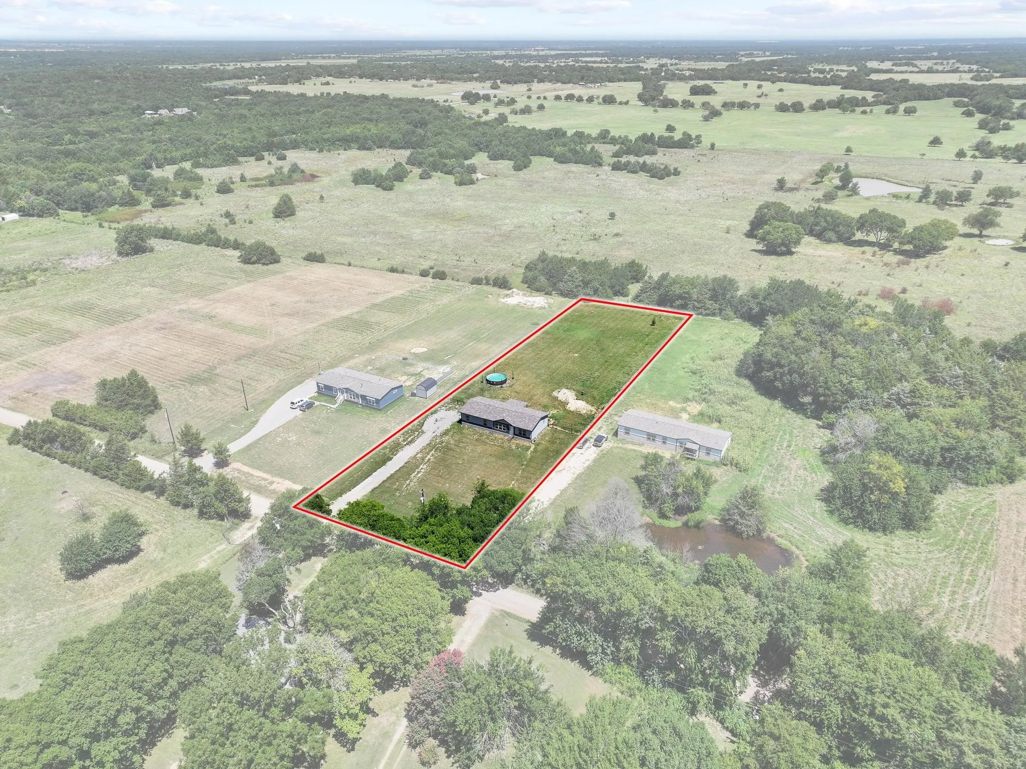 Expansive rural property featuring a single-story residence, a long driveway, surrounding open fields, and mature trees