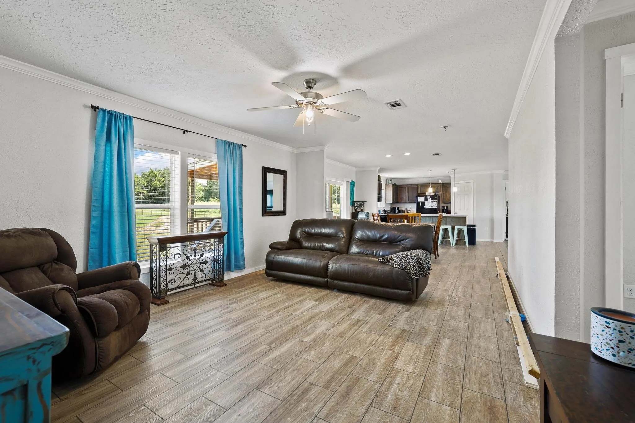 Spacious living area featuring wood-look tile flooring, white walls, and crown molding