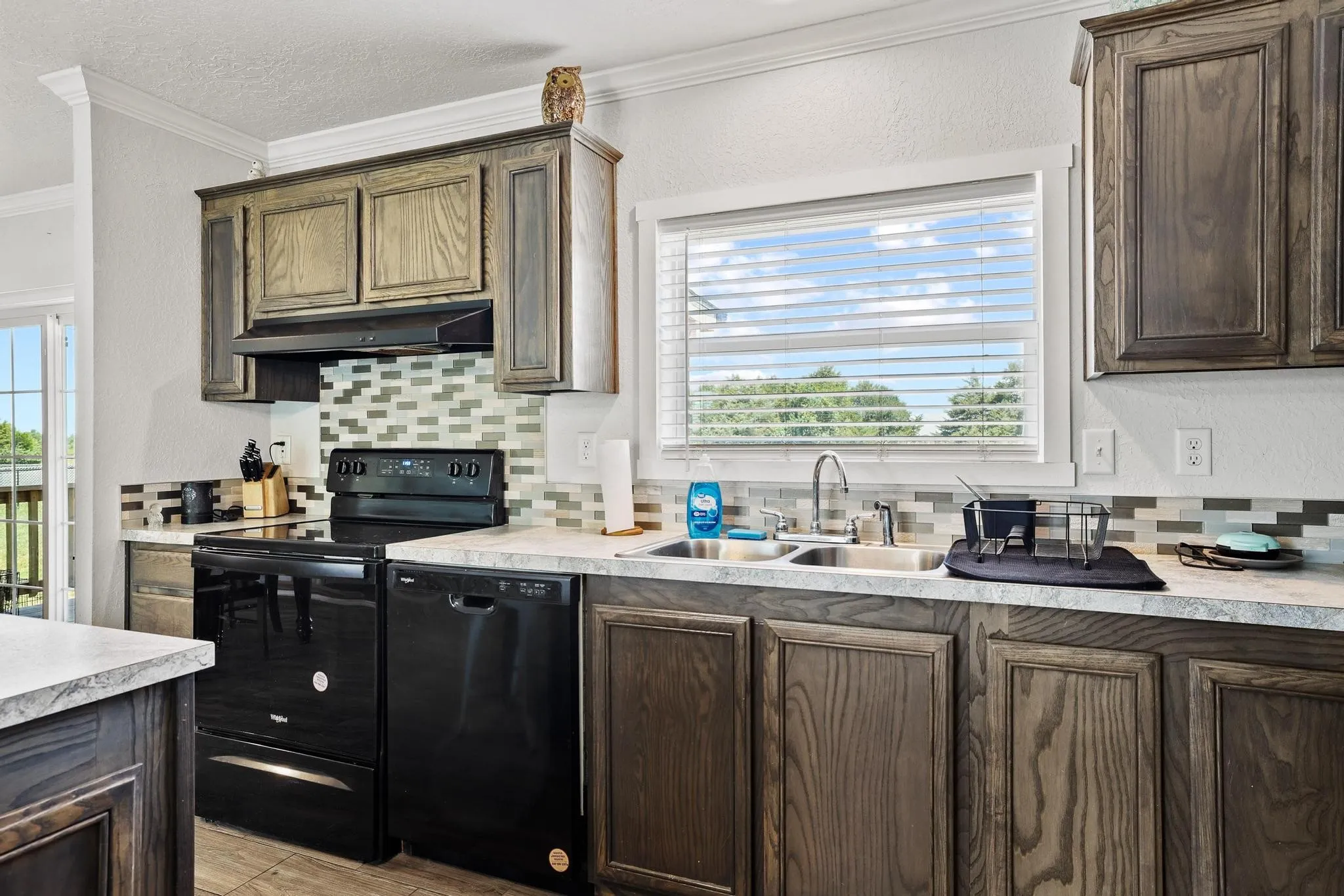 Kitchen featuring dark wood-finish cabinetry, a black appliance suite, and a stainless steel double sink with a gooseneck faucet