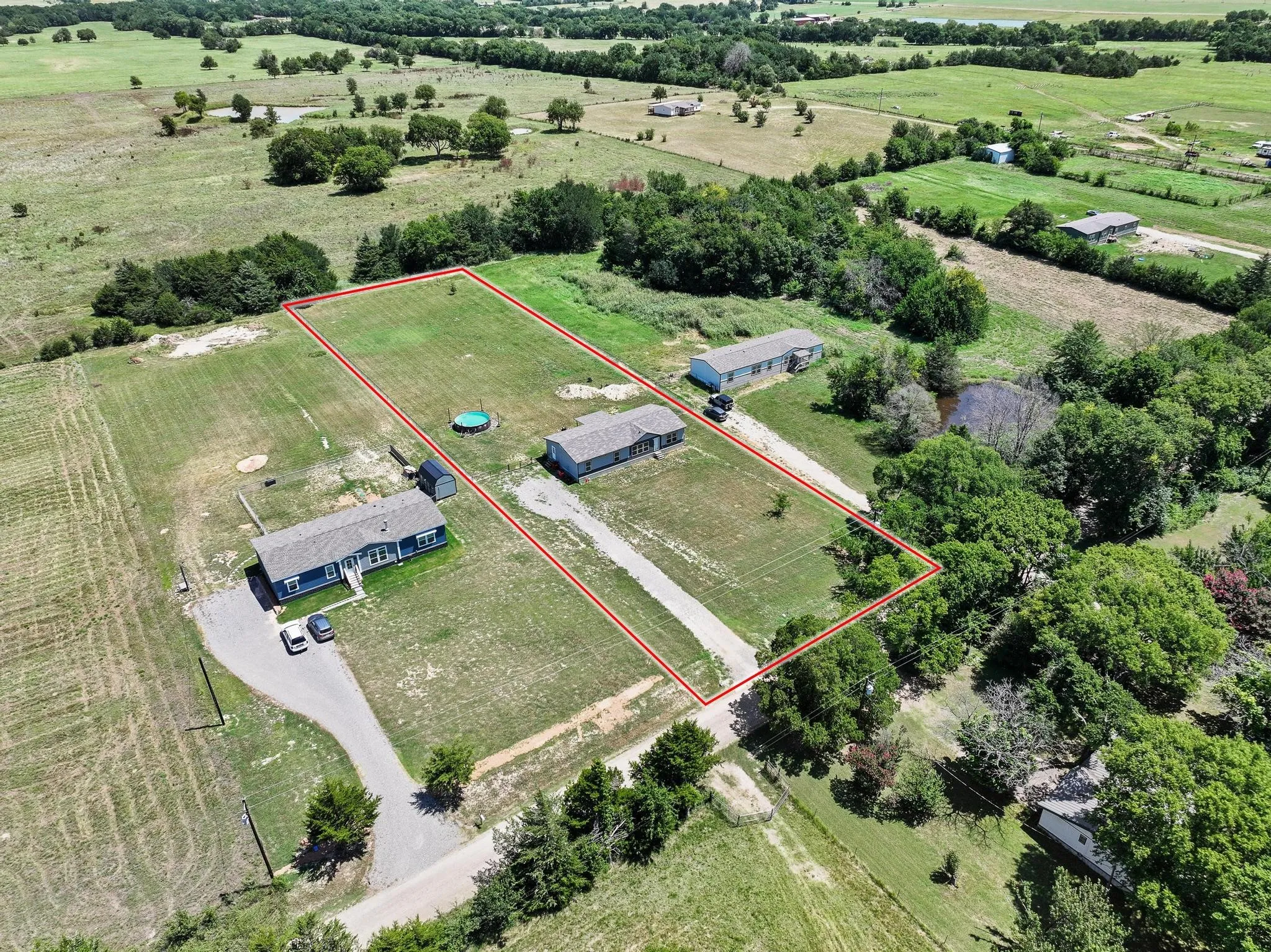 Expansive property featuring two residential structures, a long gravel driveway, a detached shed, a small pond, and abundant mature trees