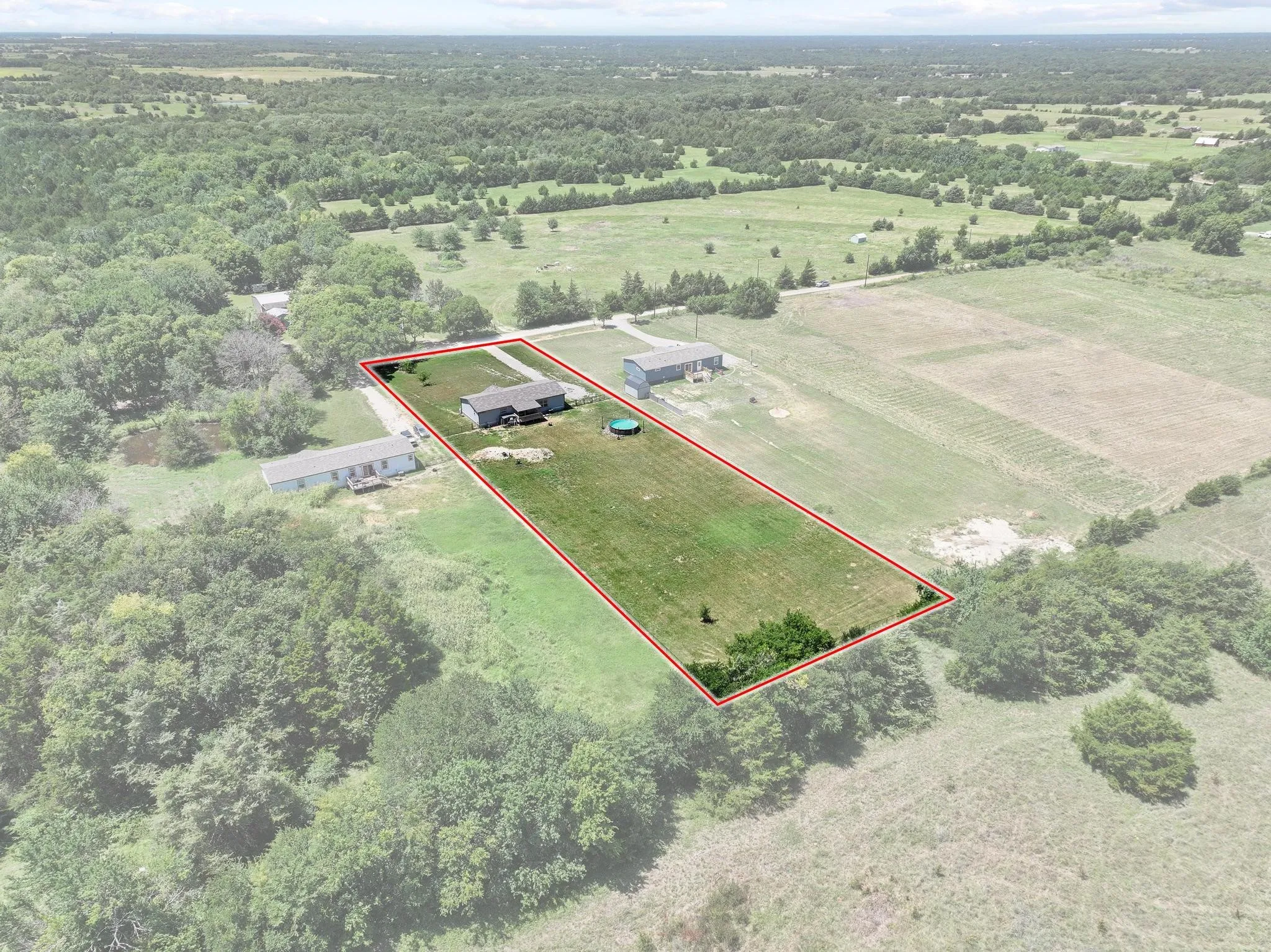 Expansive property showcasing a single-story residence and a detached auxiliary building, surrounded by open fields and mature tree lines
