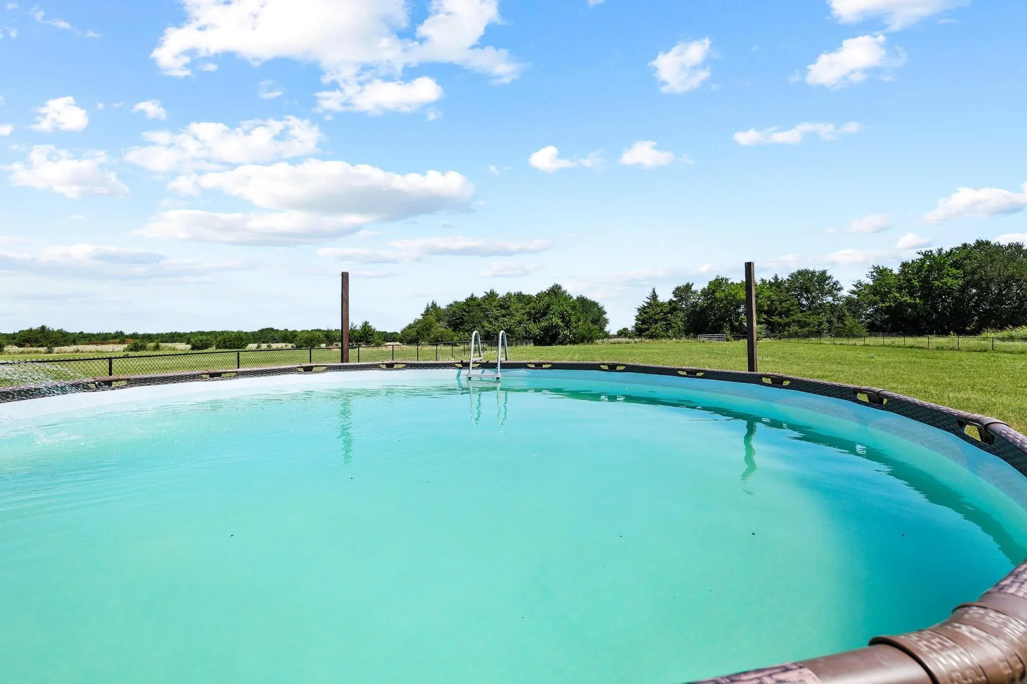 Above-ground pool with metal frame and ladder, situated on a grassy area surrounded by distant trees