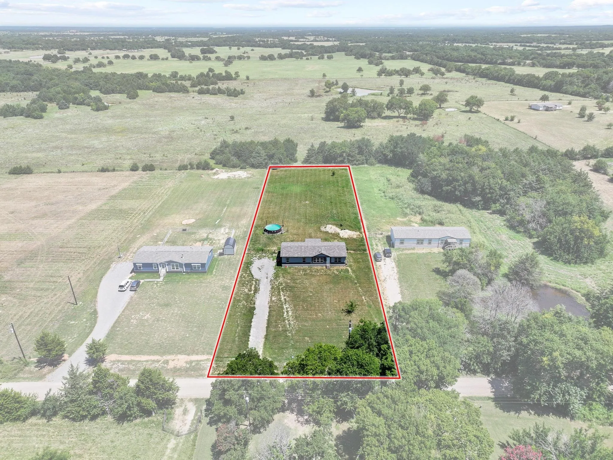 Expansive rural property featuring a single-story residence, a gravel driveway, and mature trees