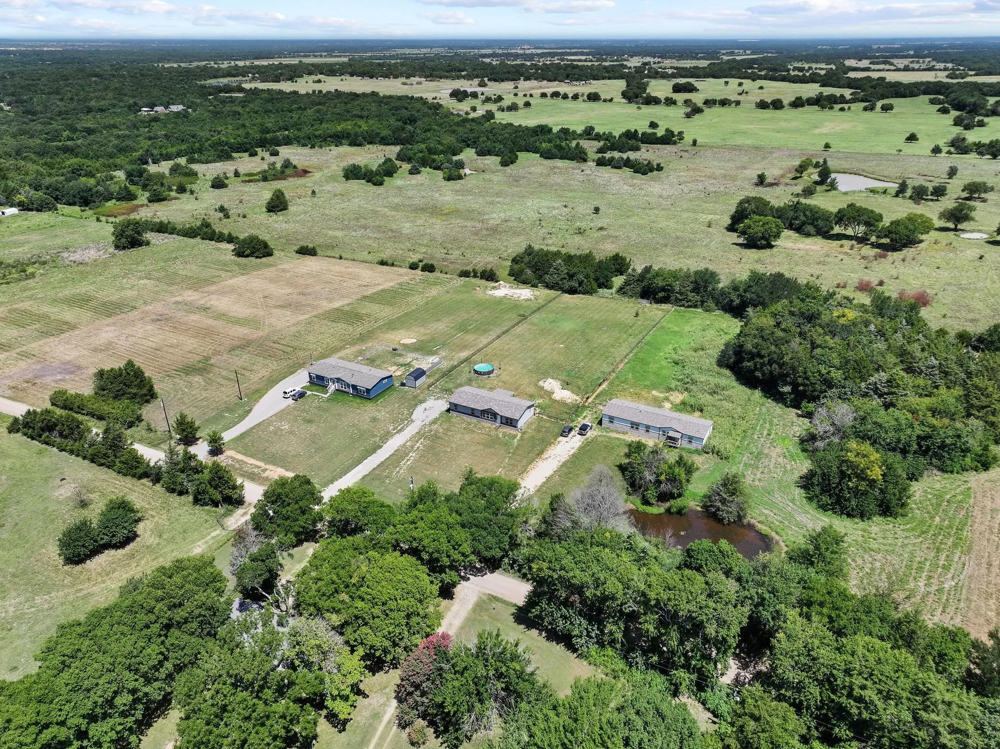 Expansive rural property featuring three structures, a private pond, mature trees, and open land