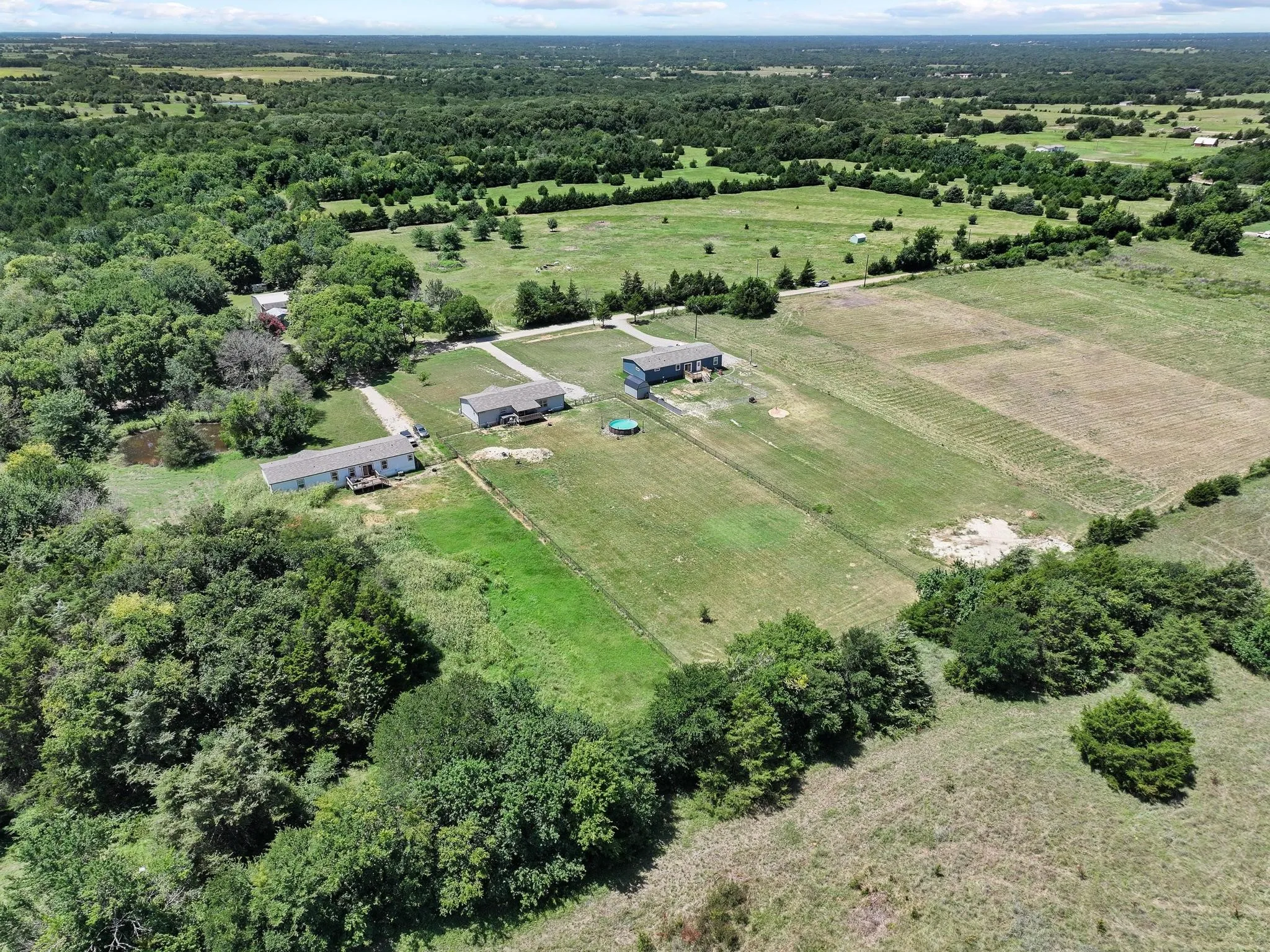 Expansive property featuring three residential structures, multiple cleared fields, and abundant mature trees