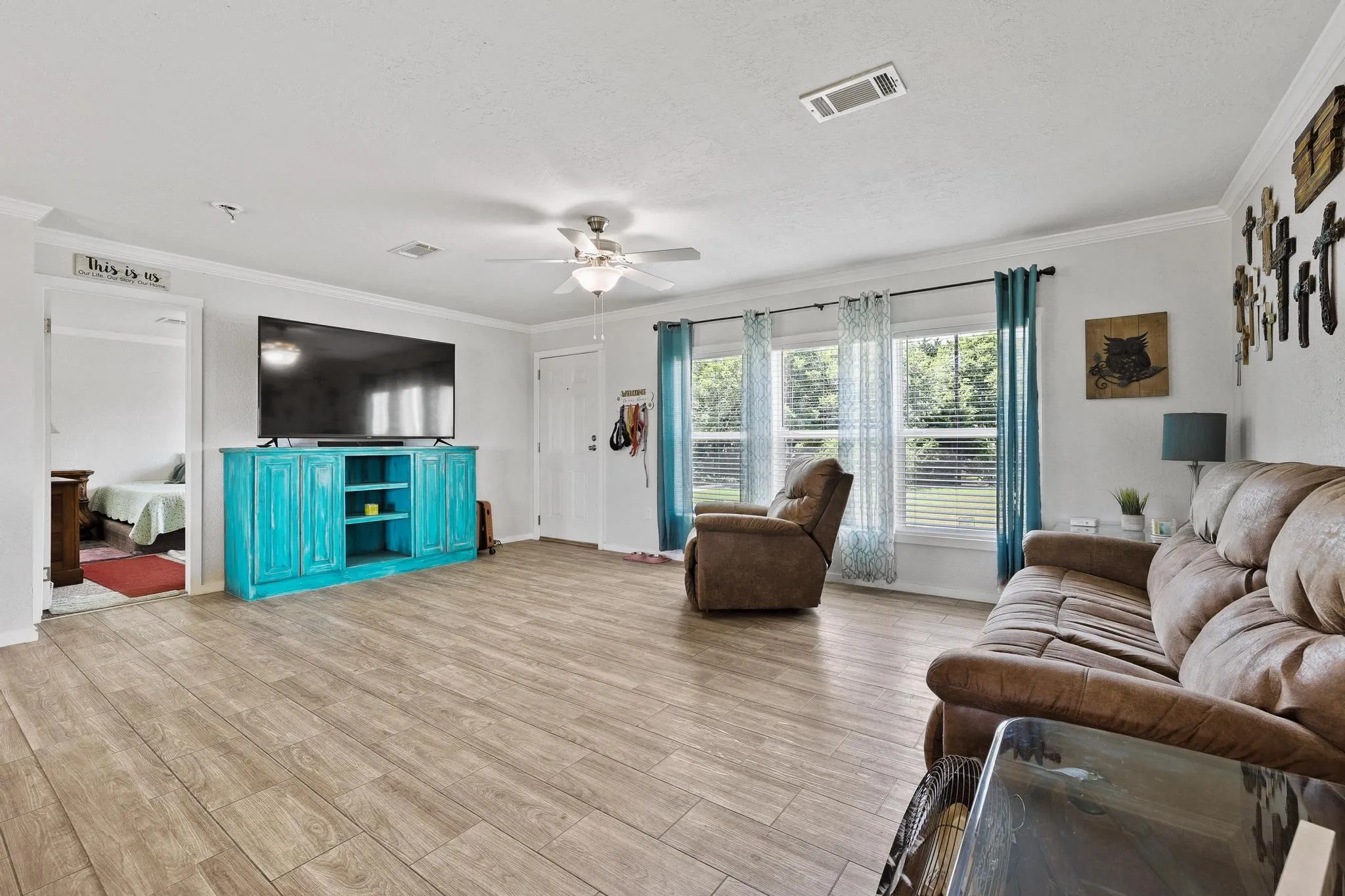 Spacious living area featuring wood-finish flooring, white crown molding, multiple windows with blinds, and an overhead ceiling fan