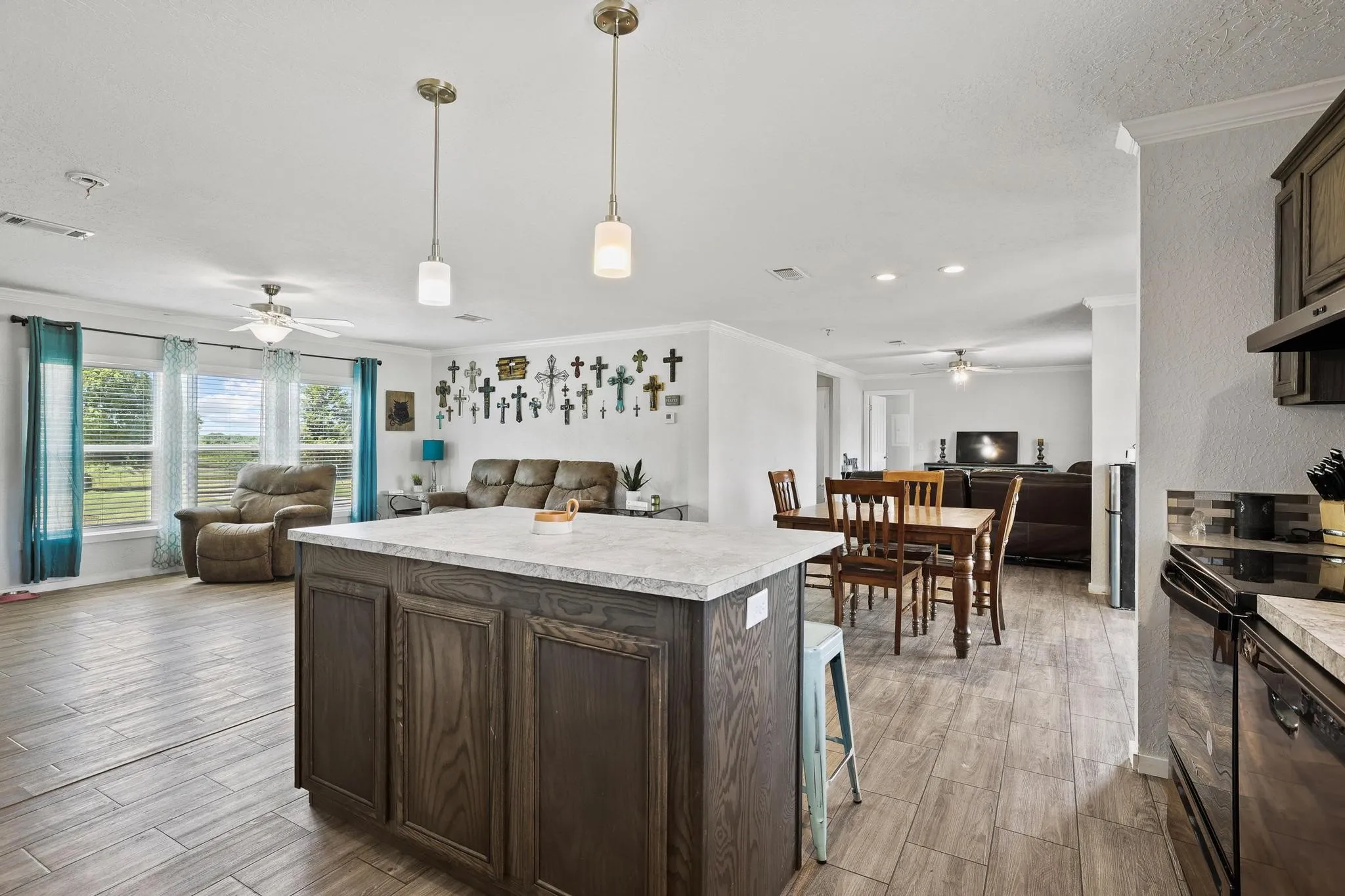 Open-concept living space featuring a kitchen island with pendant lighting, wood-finish flooring, and multiple windows offering exterior views