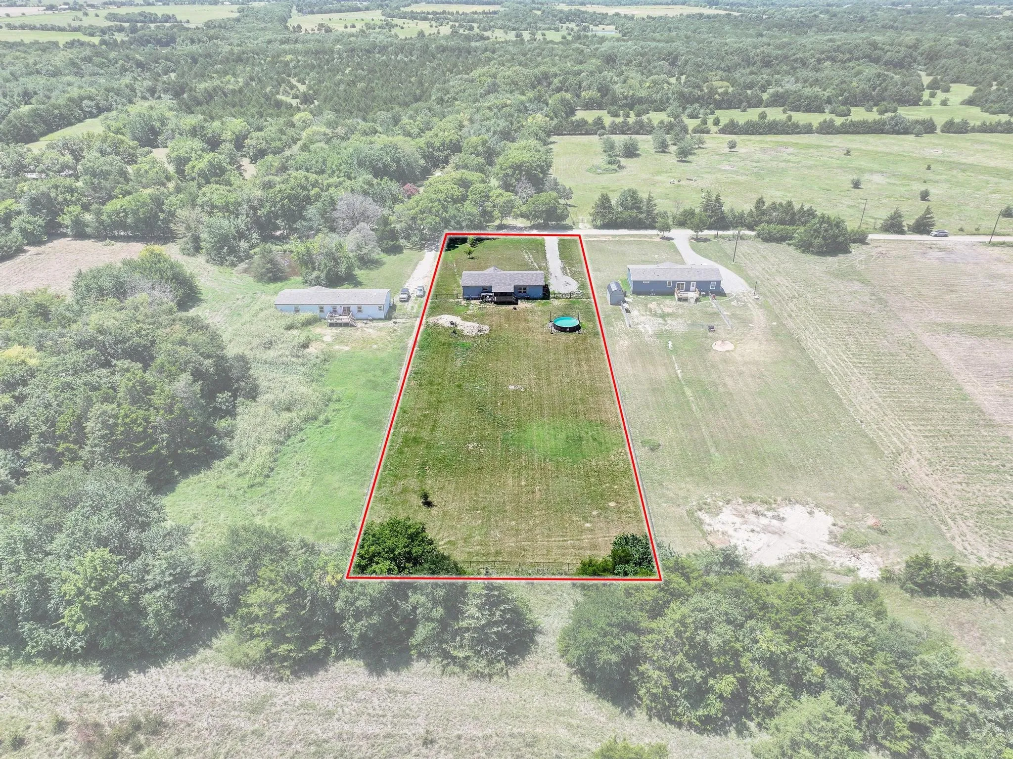 Expansive property featuring a rectangular lot outlined in red, with a single-story residence and detached outbuilding