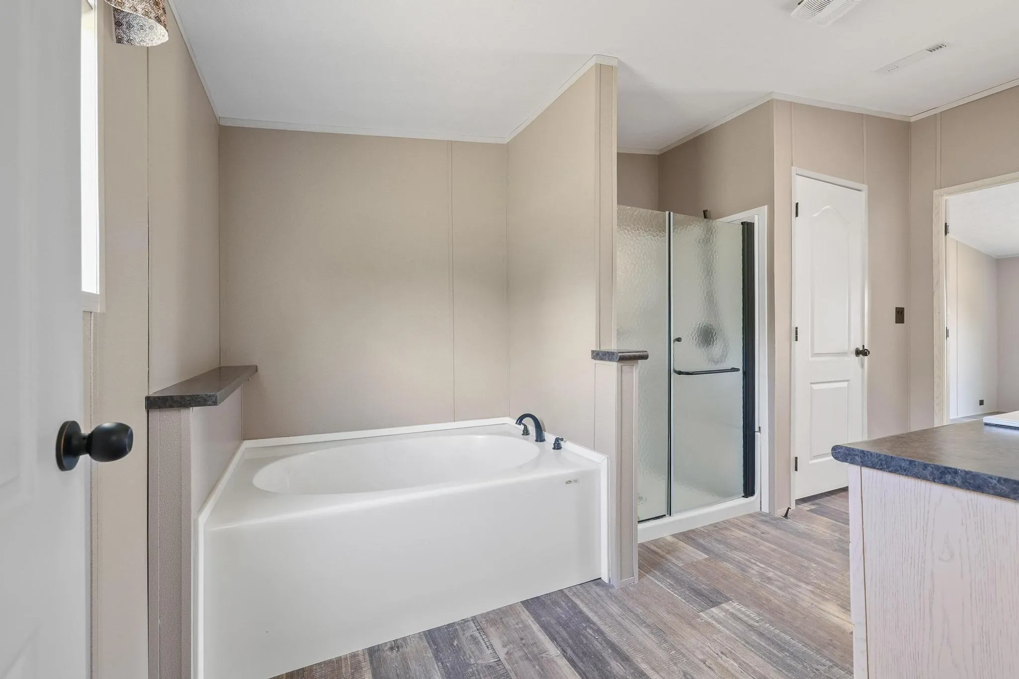 Bathroom featuring a built-in soaking tub with dark fixtures, a glass-enclosed shower, wood-finish flooring, and a window providing natural light