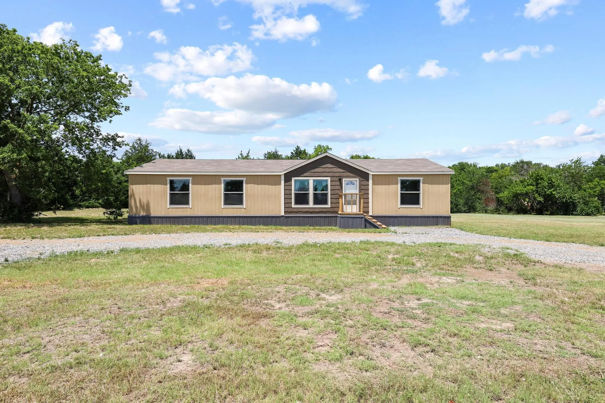 Ranch-style residence featuring a gravel driveway, mature trees, and a front entry porch with steps