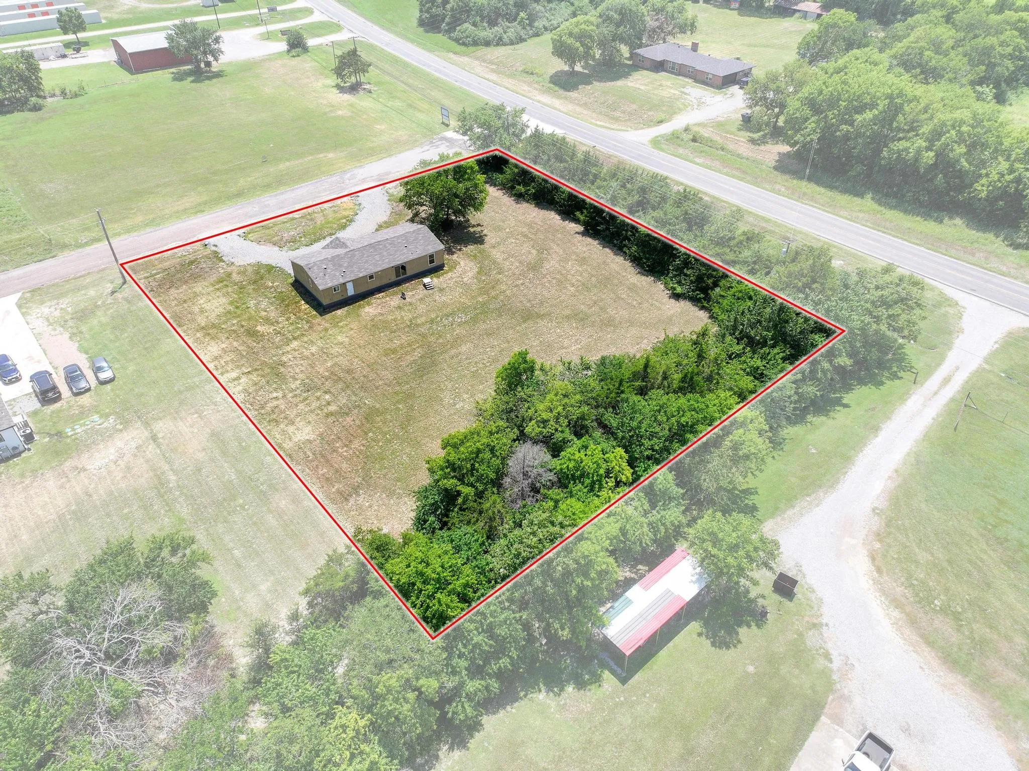 Expansive parcel featuring a single-story residence with a brown shingle roof, a gravel driveway, and mature perimeter trees