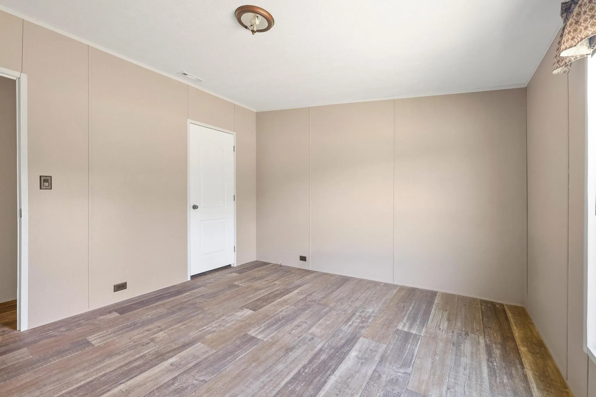 Room featuring wood-finish flooring, neutral wall paneling, a white interior door, and a ceiling-mounted light fixture
