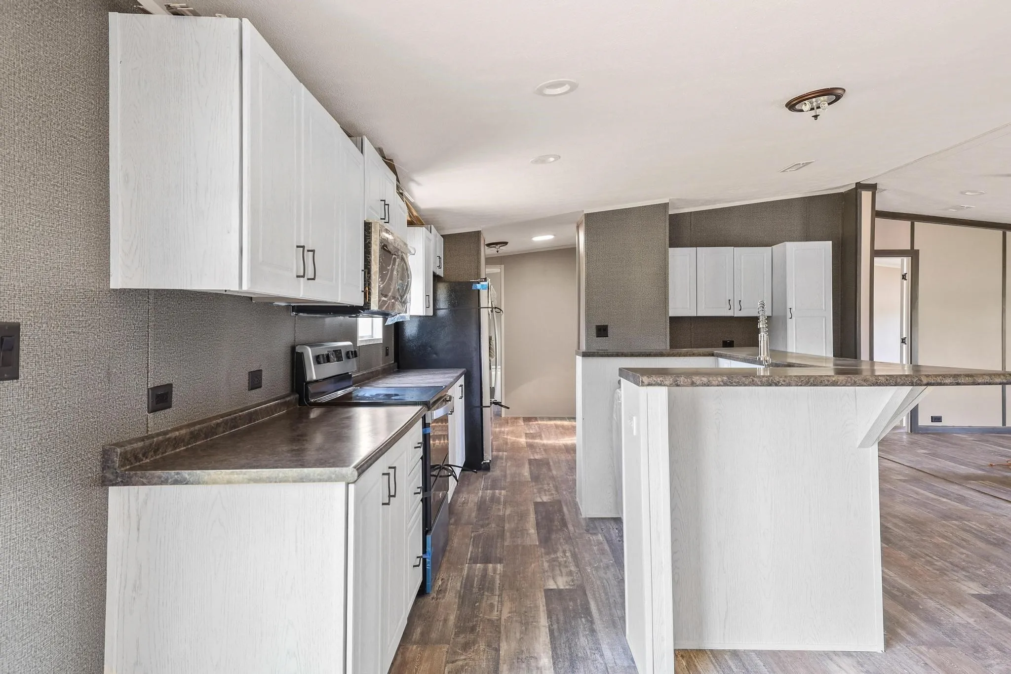 Kitchen featuring white cabinetry with dark hardware, dark countertops, and stainless steel appliances