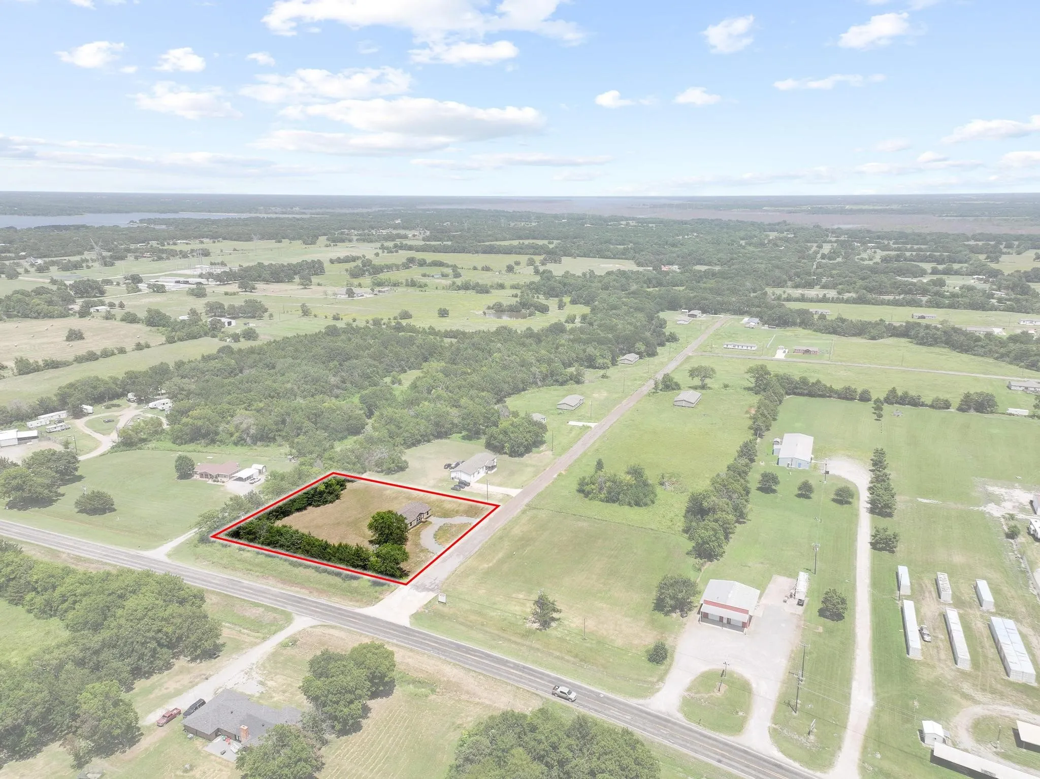 Expansive rural property featuring a single-story residence, mature perimeter trees, a paved driveway, and open grassy areas
