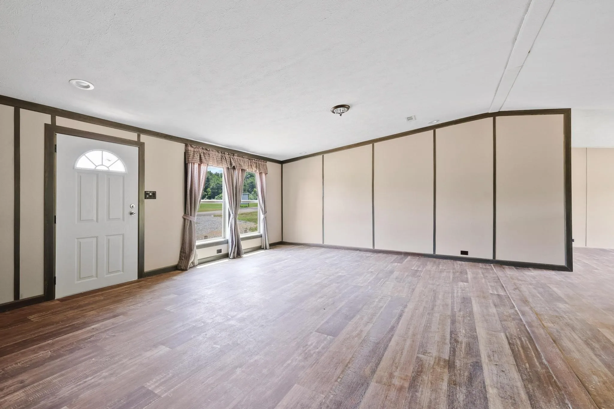 Spacious room featuring wood-finish flooring, a white paneled entry door with an arched transom, and recessed lighting