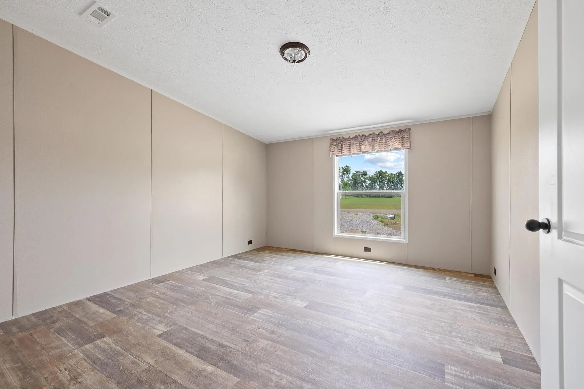 Spacious room featuring wood-finish flooring, light-toned wall panels, and a prominent window