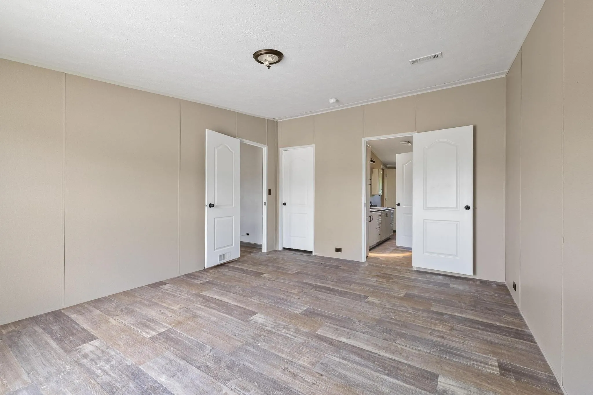 Spacious room featuring wood-finish flooring, neutral wall paneling, and a flush mount ceiling light fixture