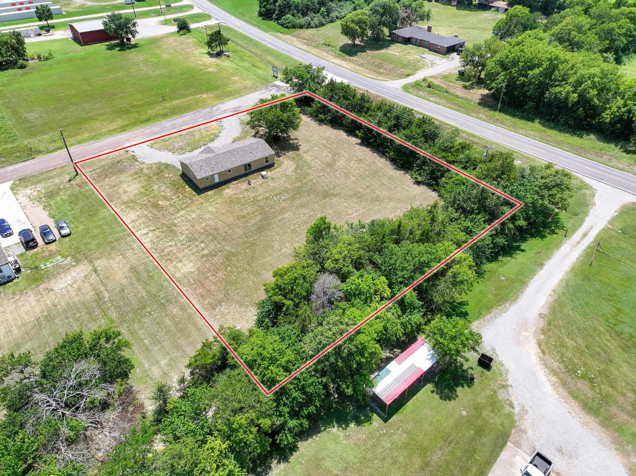 Aerial perspective showcasing a single-story dwelling with a light-colored exterior and a gray shingled roof, situated on a large grassy lot