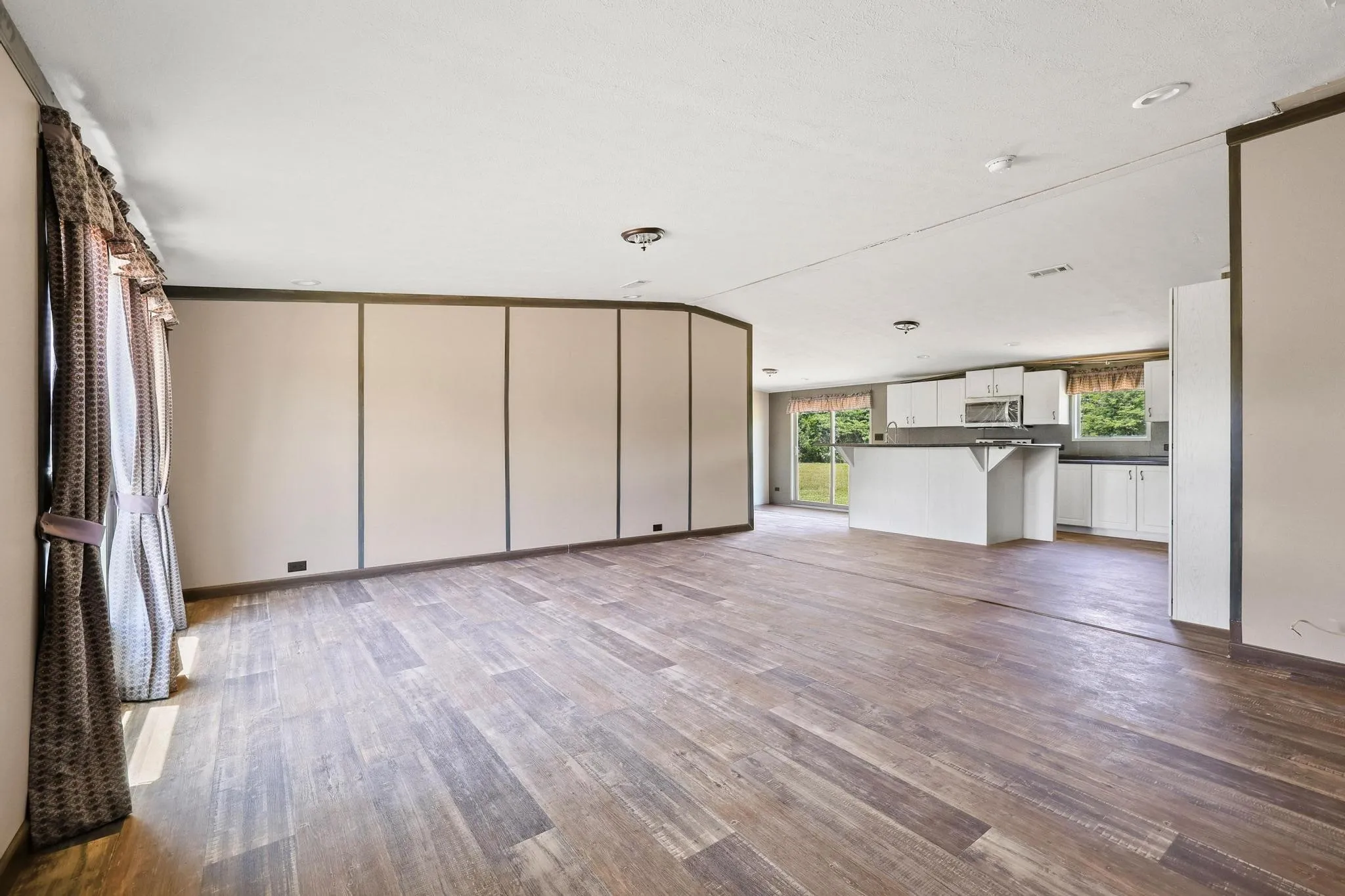 Open-concept living space featuring wood-finish flooring, a neutral color palette, ceiling-mounted lighting, and a kitchen area with white cabinetry and a breakfast bar