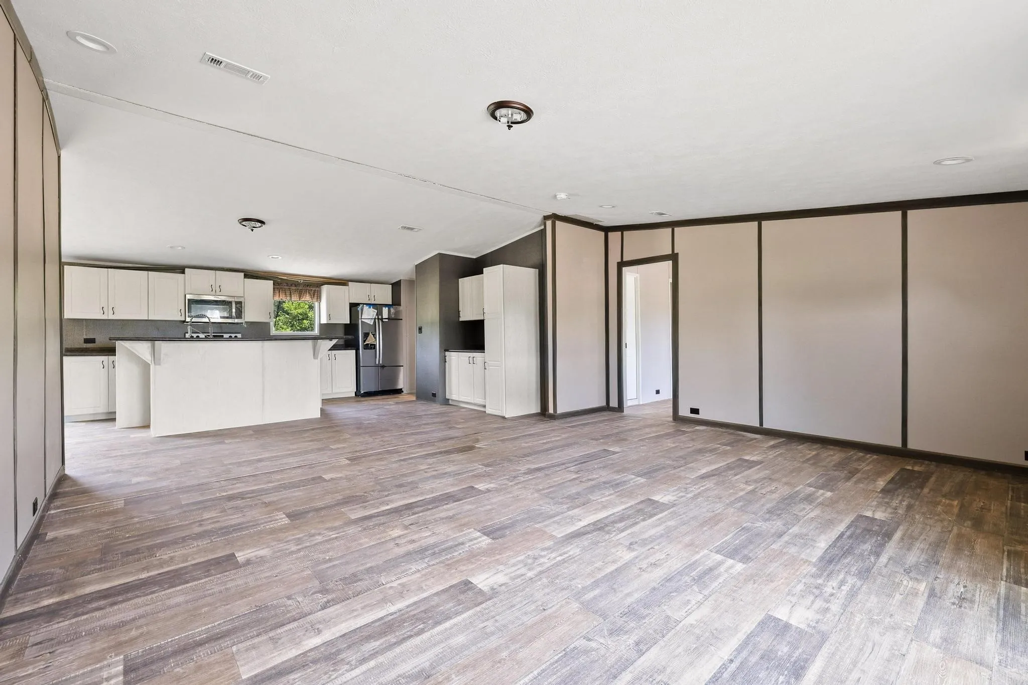 Spacious open-concept interior featuring wood-finish flooring, a kitchen island with seating, stainless steel appliances, white cabinetry, and recessed lighting