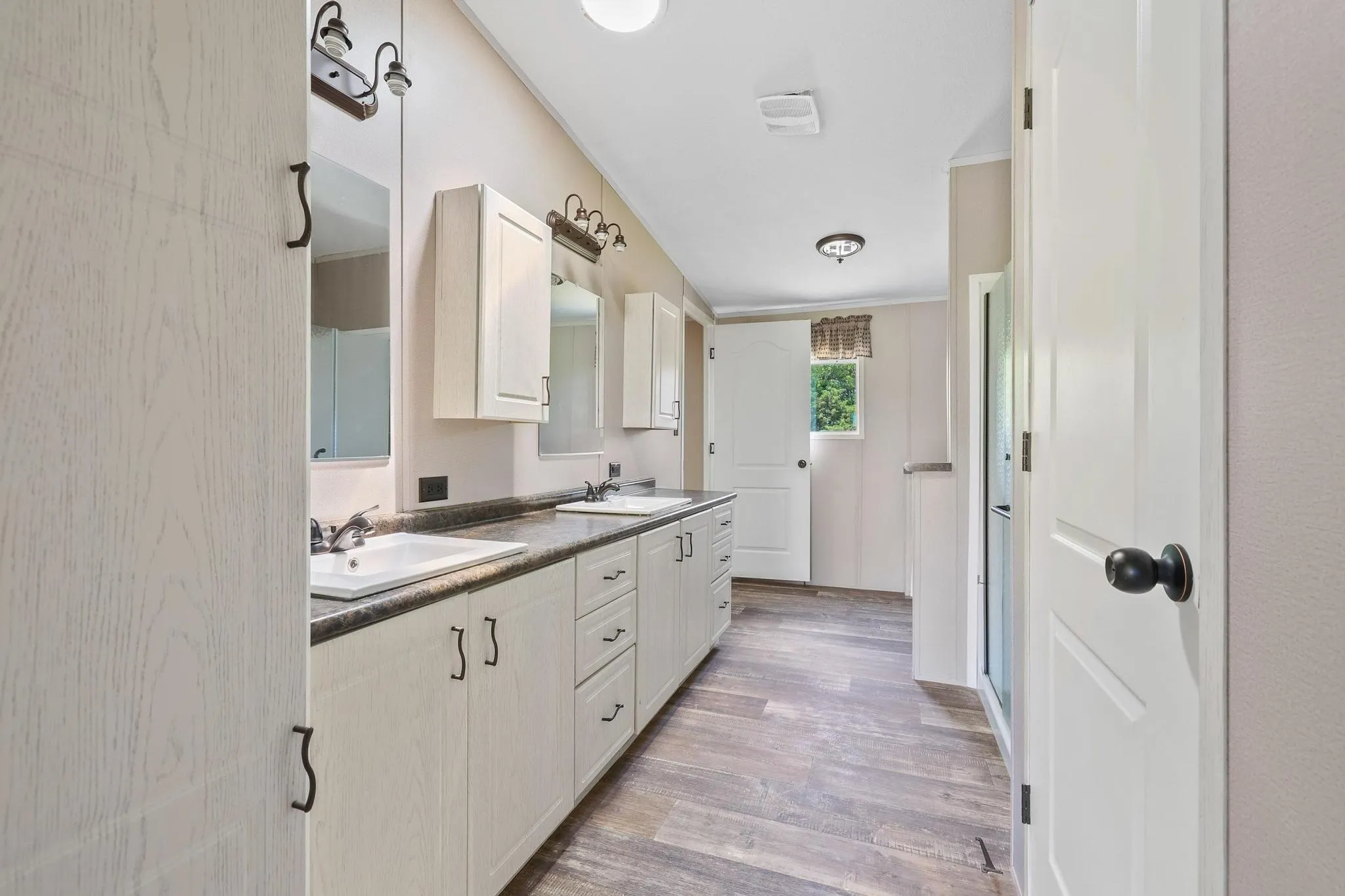 Dual vanity with white cabinetry and dark countertops, individual mirrors, and wood-finish flooring